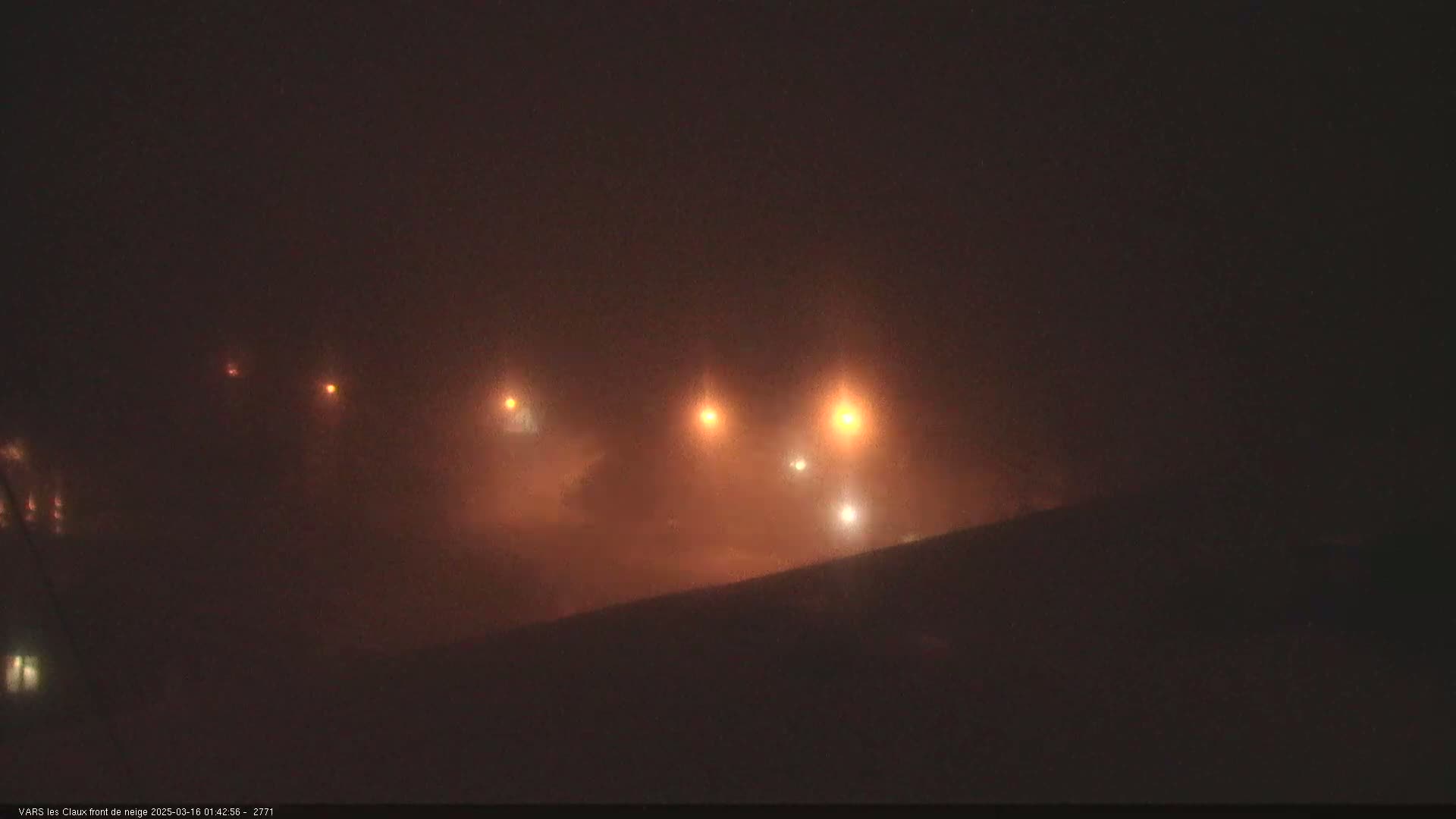 Faintly lit vehicles are barely visible through a thick fog at night.