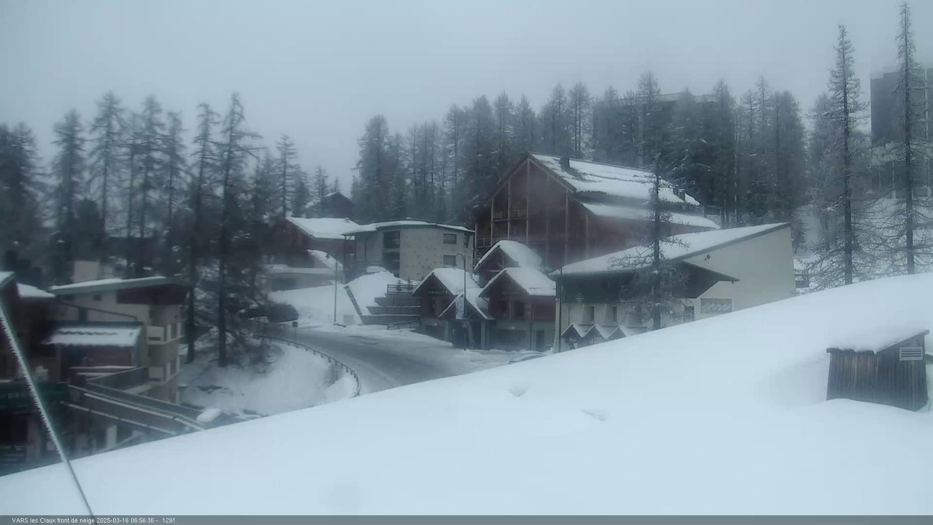 Snow-covered buildings and trees are visible in a snowy, overcast mountain setting.