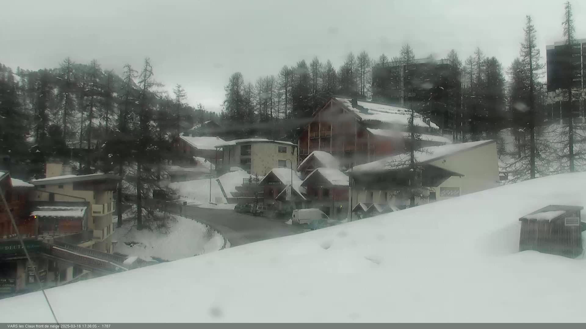 A snow-covered village nestled among evergreen trees in overcast weather.