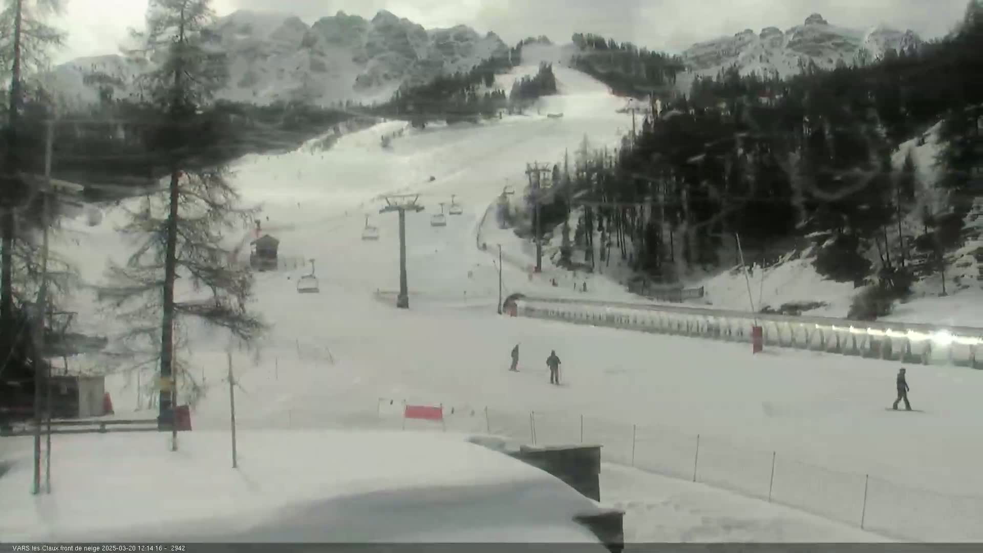 A snow-covered ski slope with several skiers and chairlifts is visible under an overcast sky.