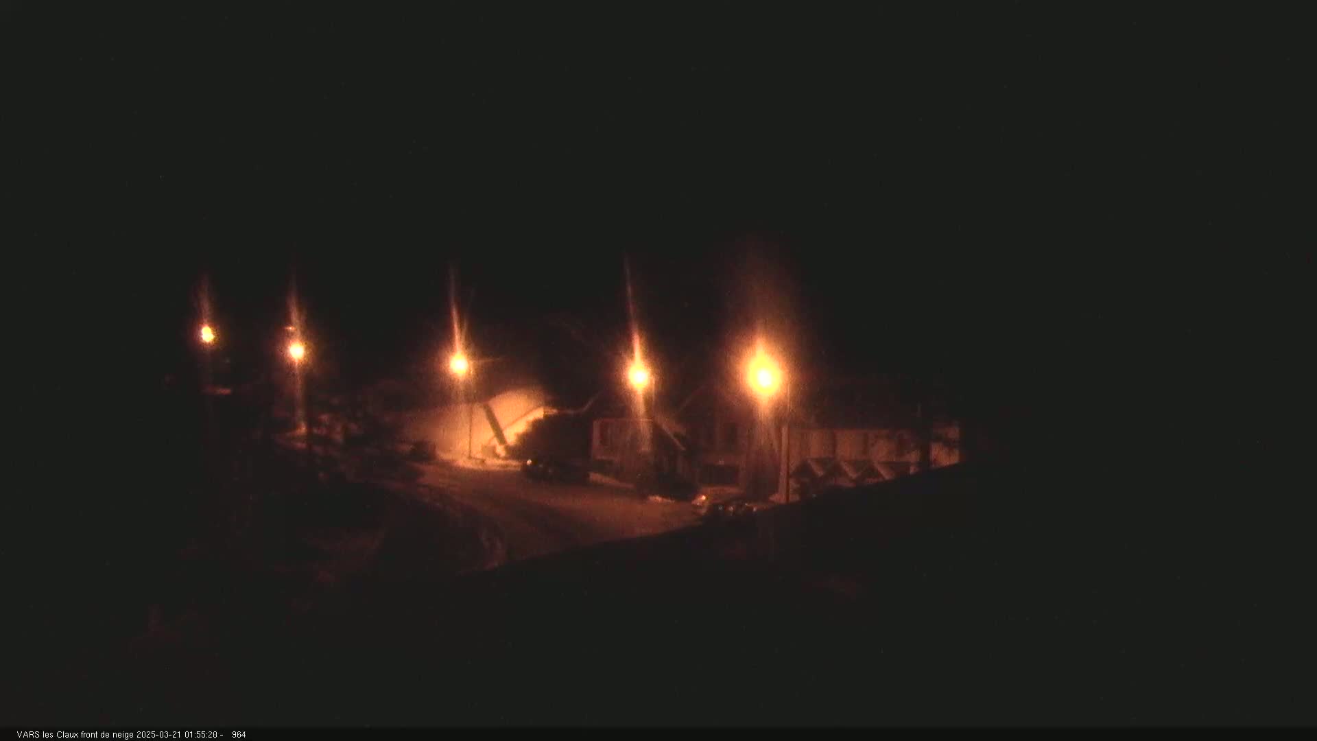 At night, several illuminated streetlights cast light on a snow-covered street and buildings.