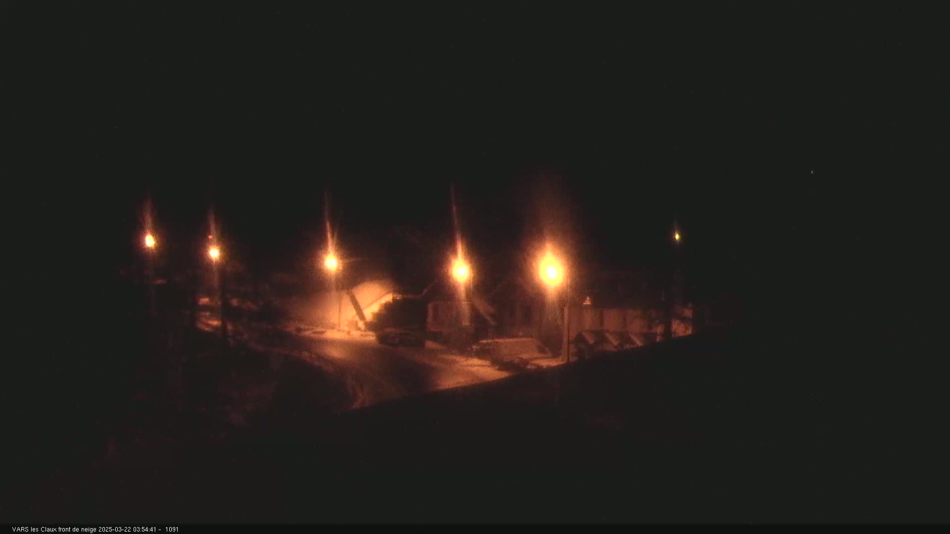 Several illuminated streetlights cast light on a snow-covered area at night.