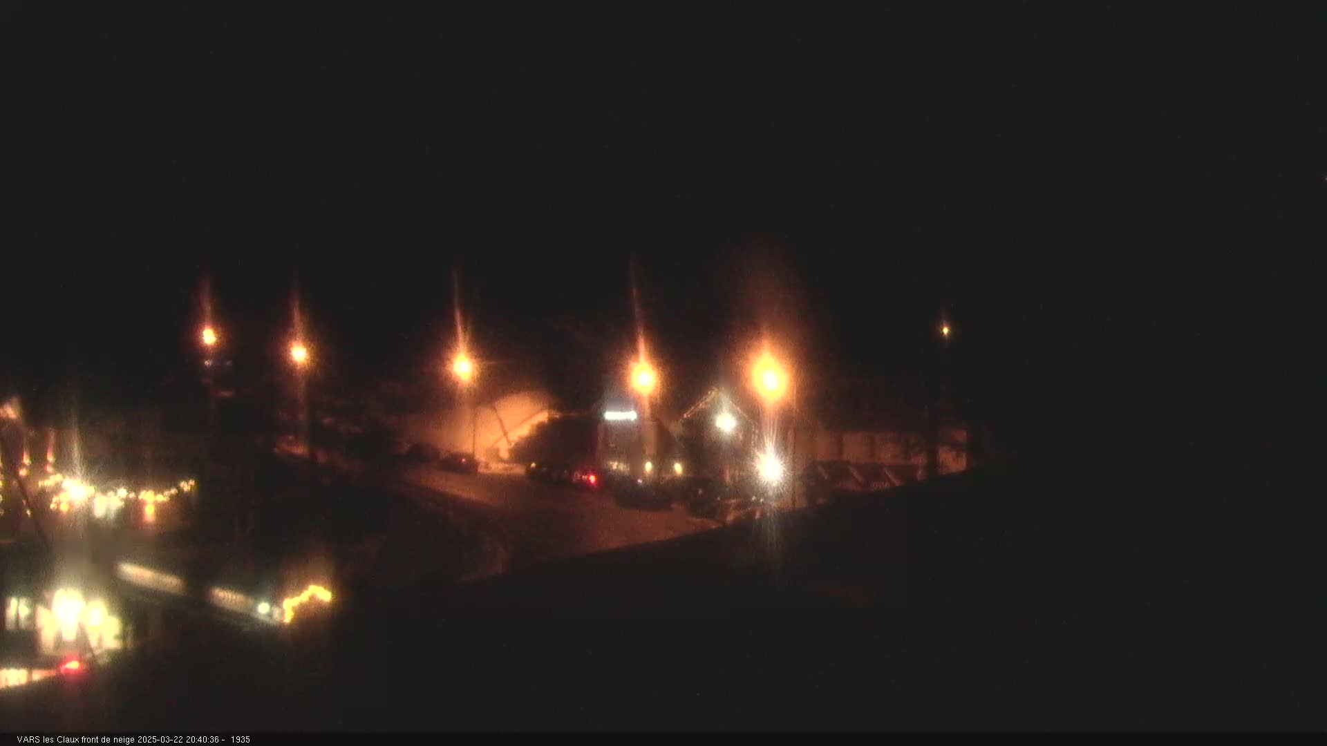 A nighttime view of a snow-covered area with several illuminated buildings and streetlights.