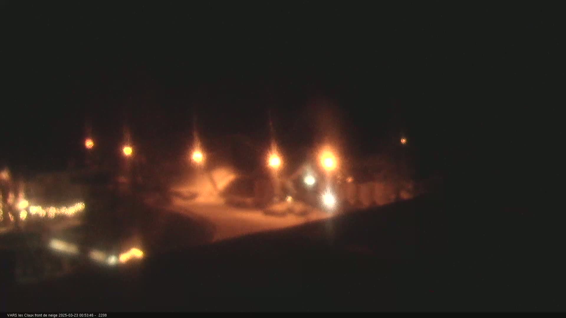 A nighttime scene shows blurry lights from street lamps and vehicles in snowy conditions.