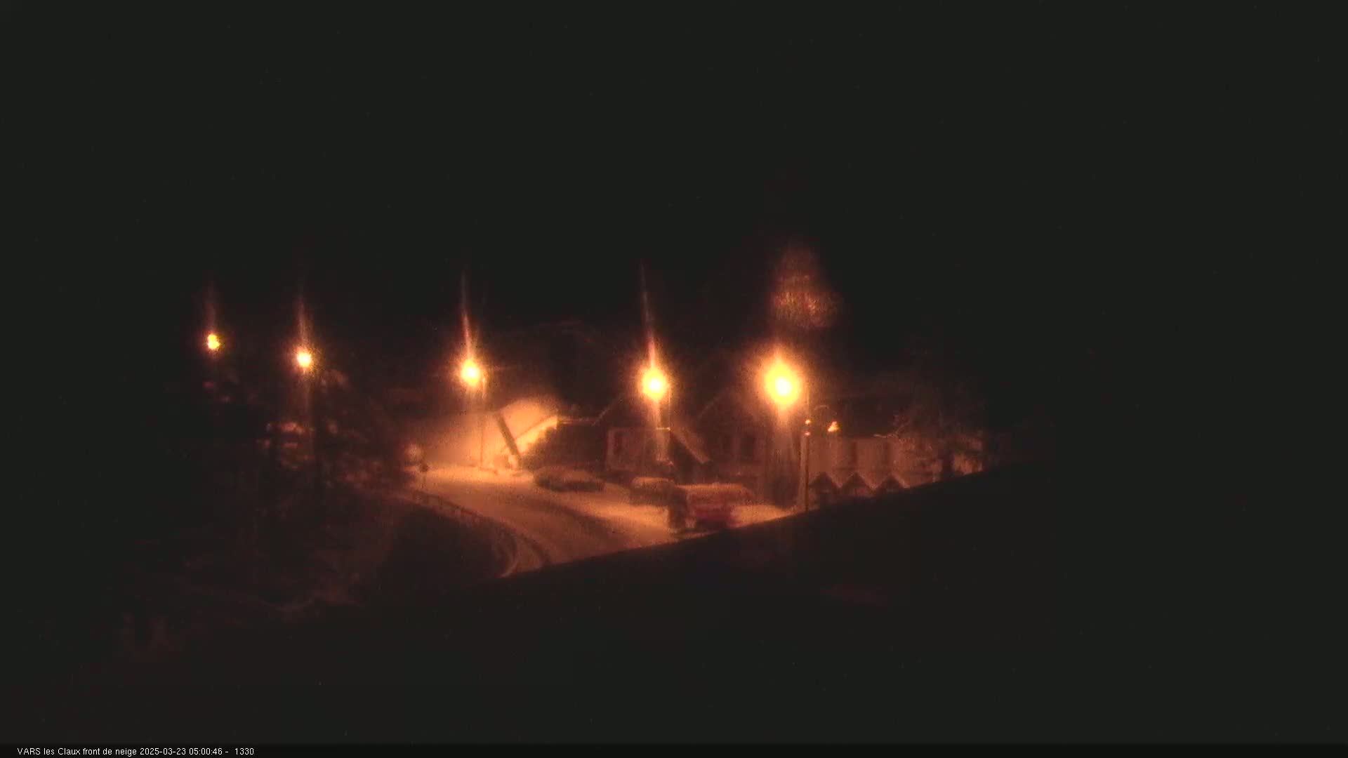 A nighttime view of a snow-covered road and buildings illuminated by streetlights.