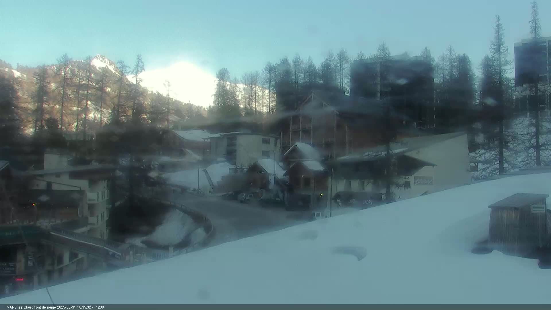 A snow-covered village nestled in a valley, with mountains in the background under a mostly clear sky.