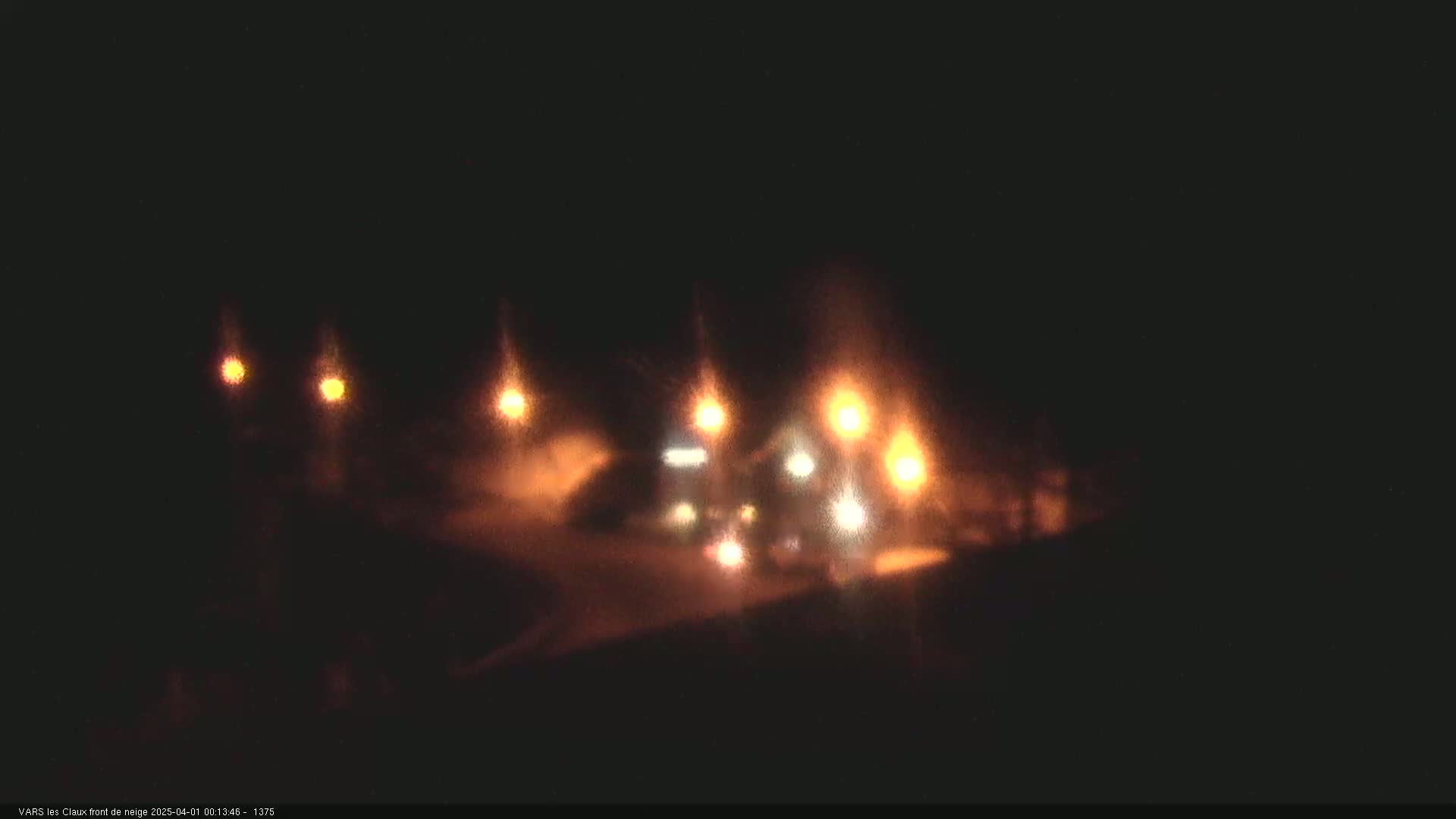 At night, blurry lights illuminate a snow-covered area with vehicles.