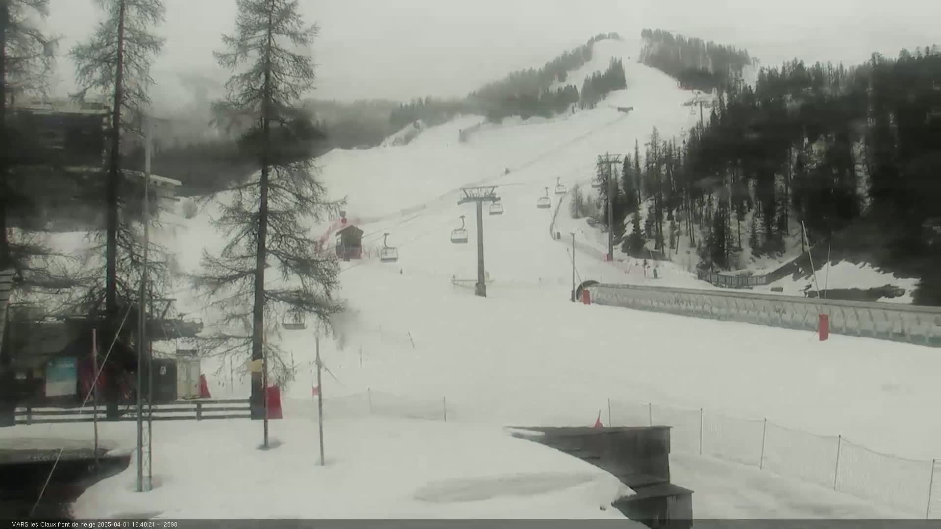 A snow-covered ski slope with a chairlift and several evergreen trees is visible in overcast conditions.