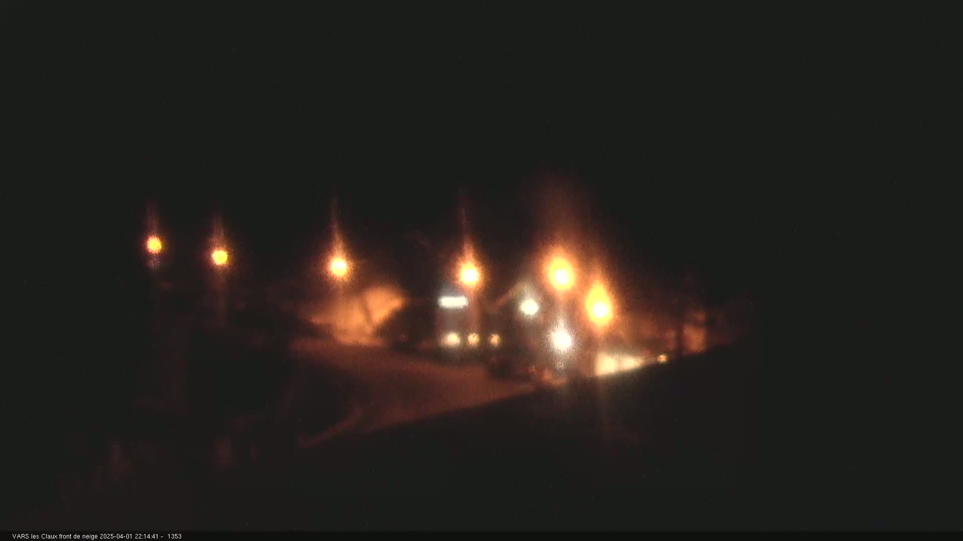 A nighttime, snowy scene shows several blurry lights illuminating a building and surrounding area.