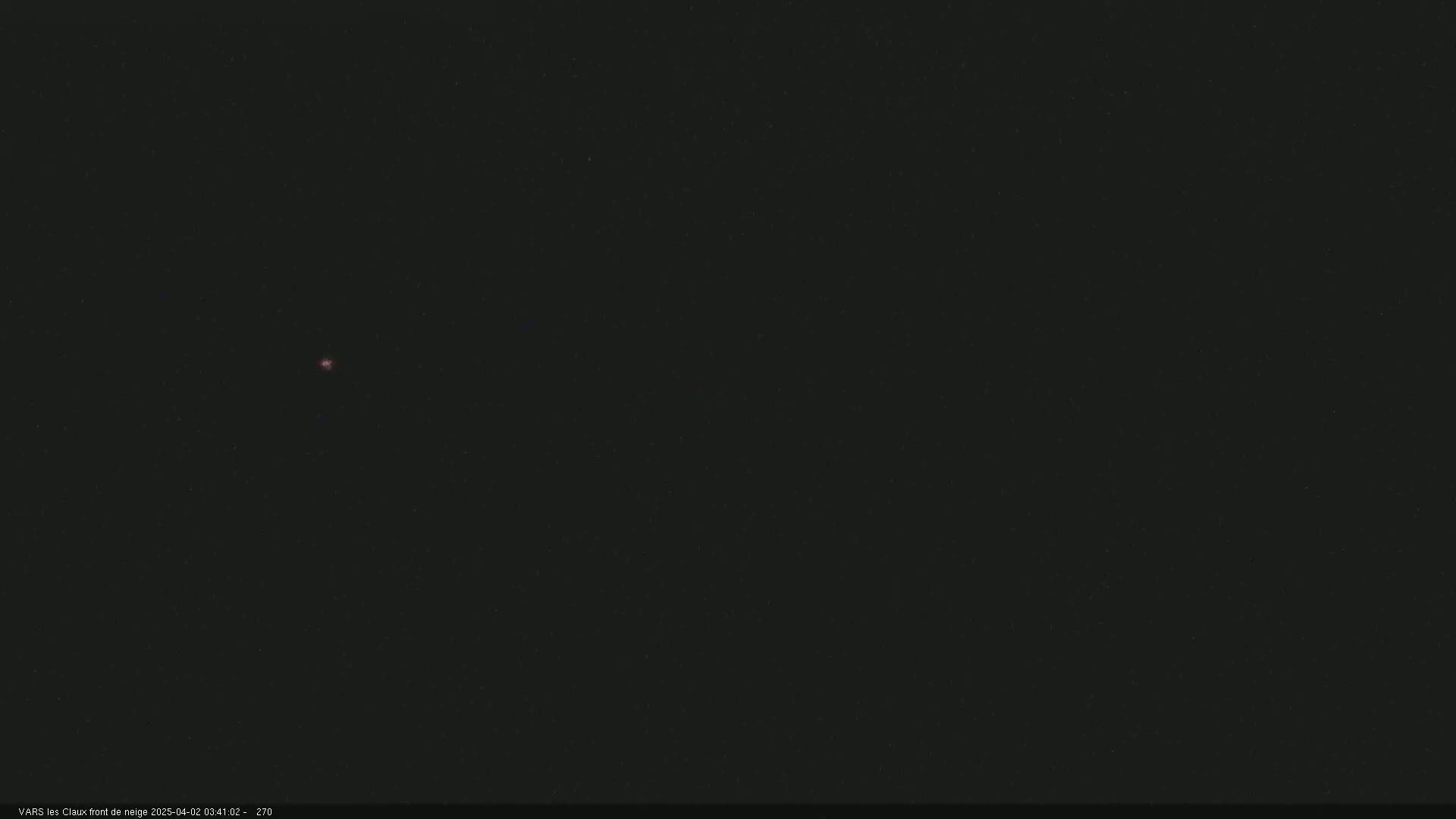 A small, faint, reddish light is visible in a dark, nighttime sky.