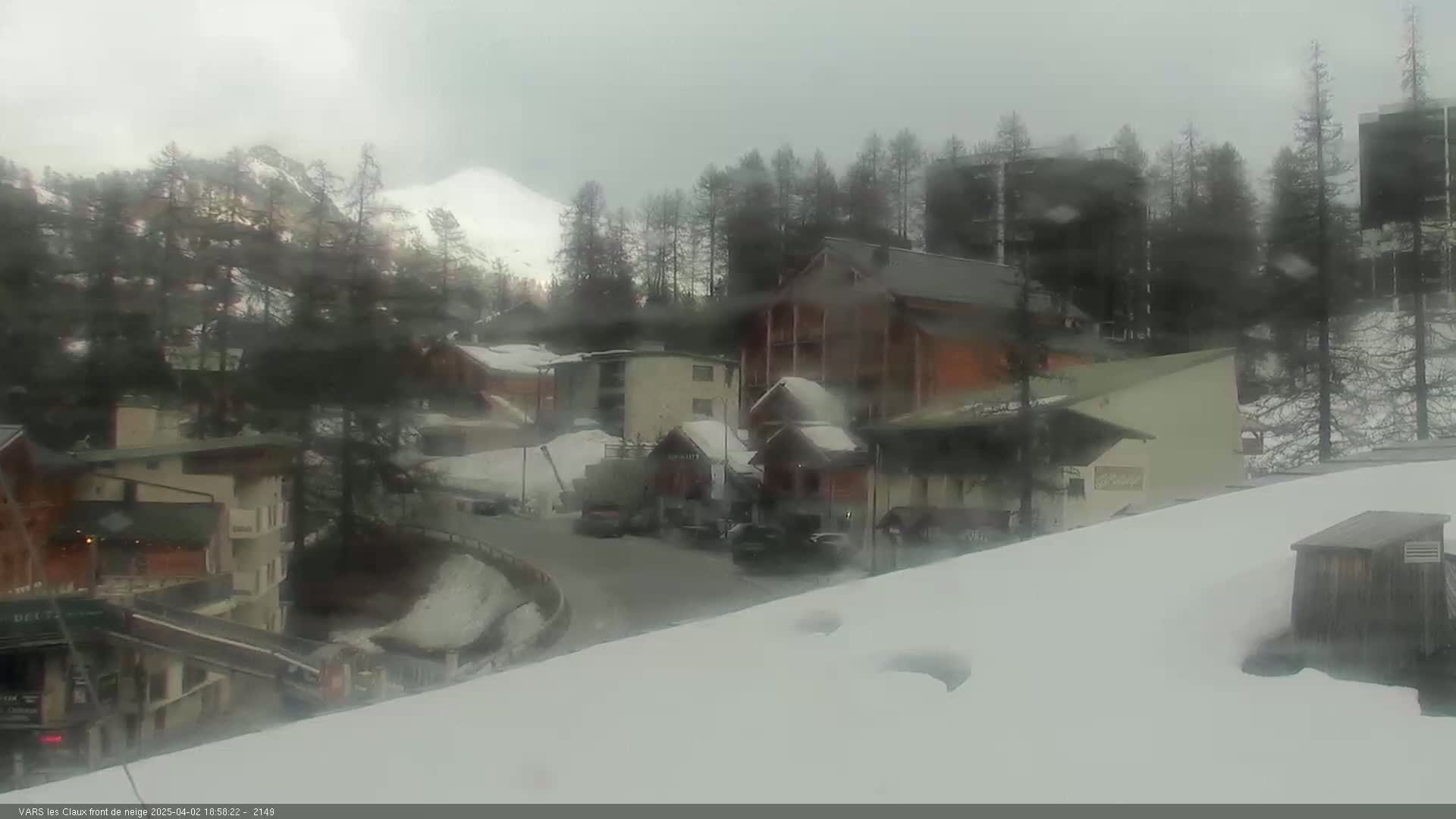 A snow-covered village nestled in a mountainous area, under a cloudy, overcast sky.
