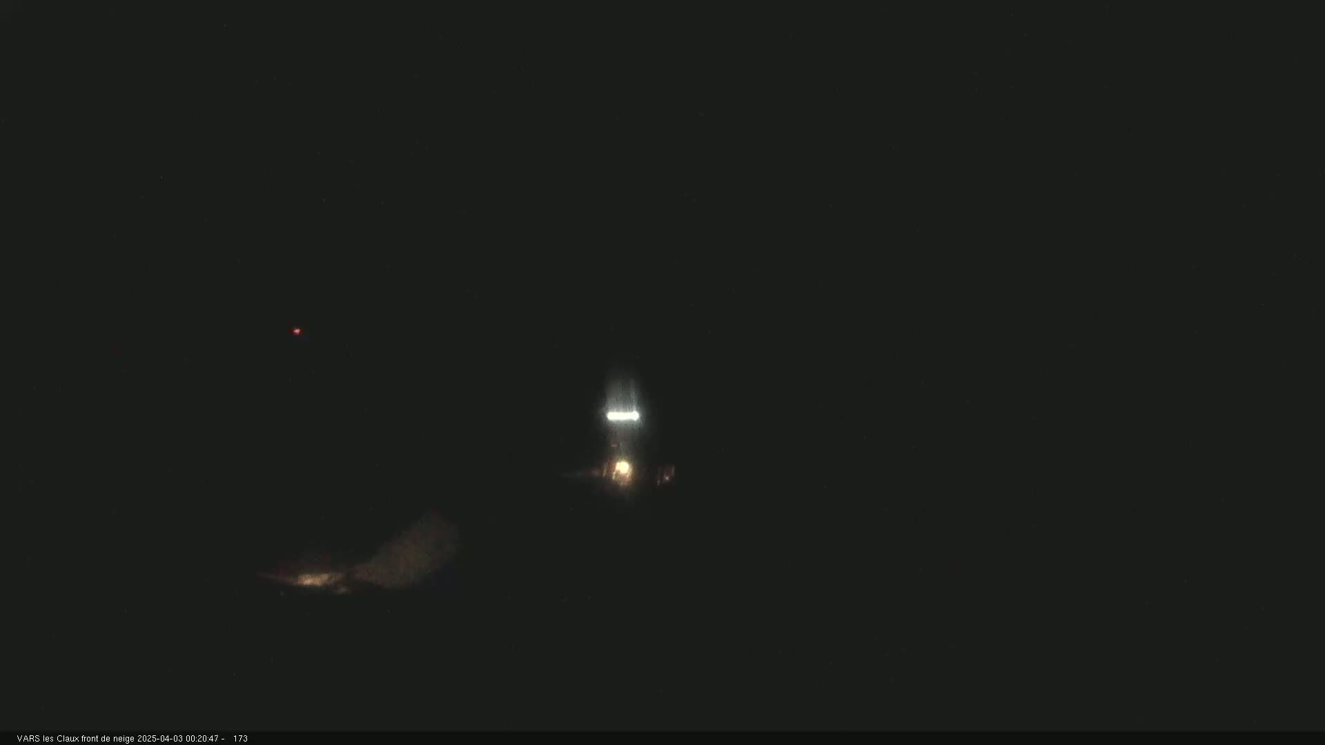 A nighttime, low-light image shows a vehicle's headlights illuminating a dark, snow-covered landscape.