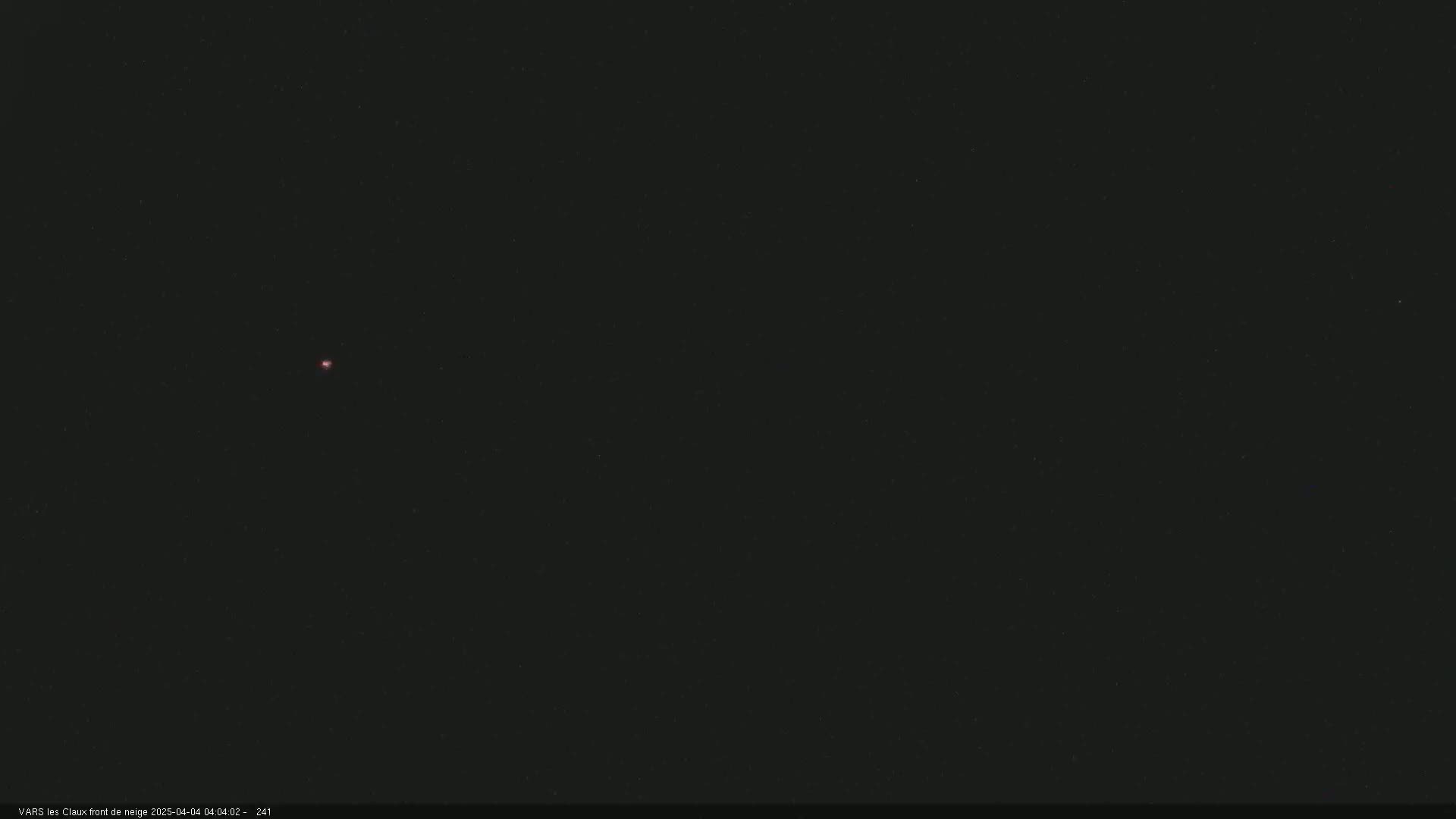 A small, faint, reddish light is visible in a dark, nighttime sky.