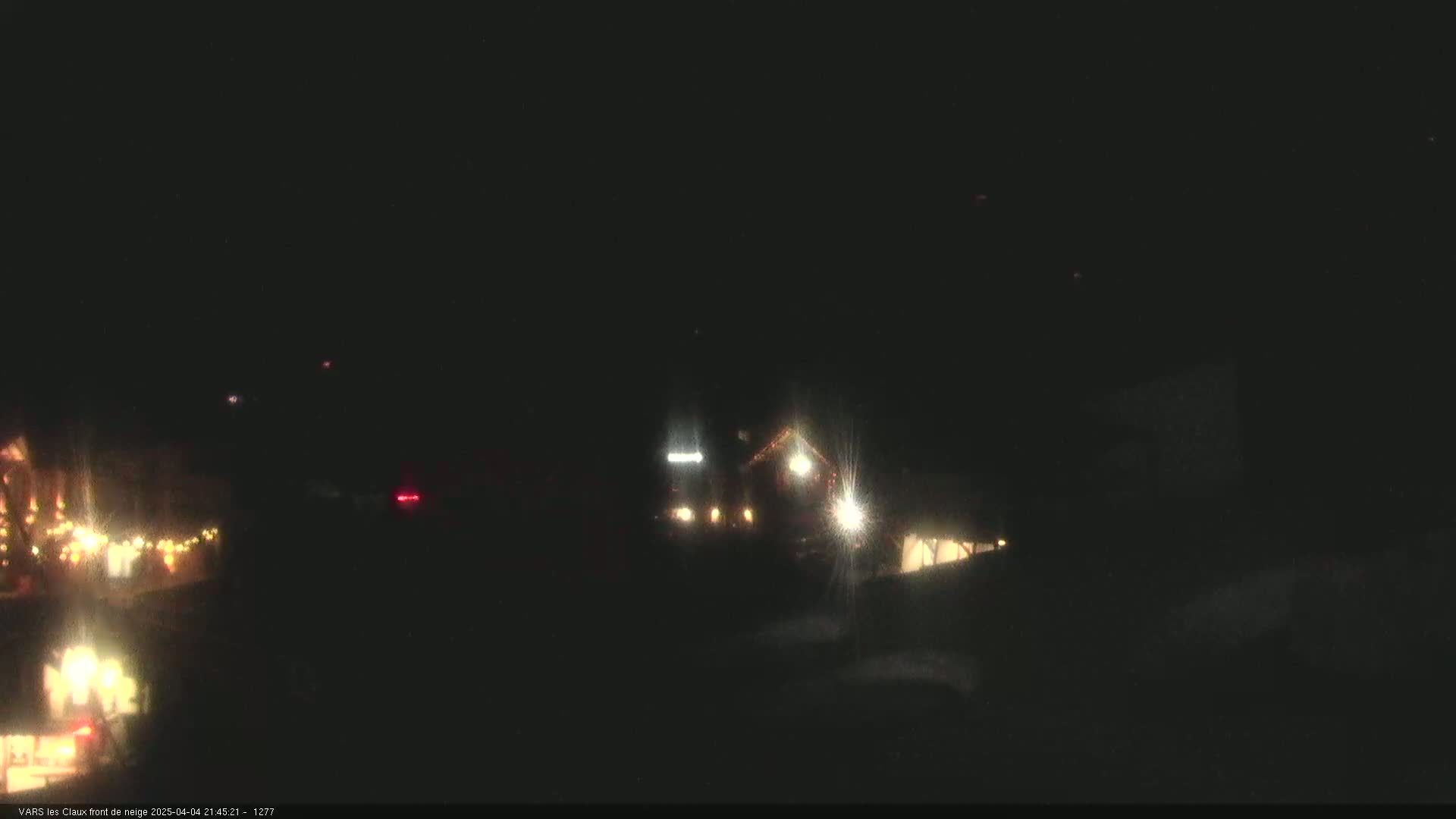 At night, a dimly lit building and some vehicles are visible in the distance under a dark sky.