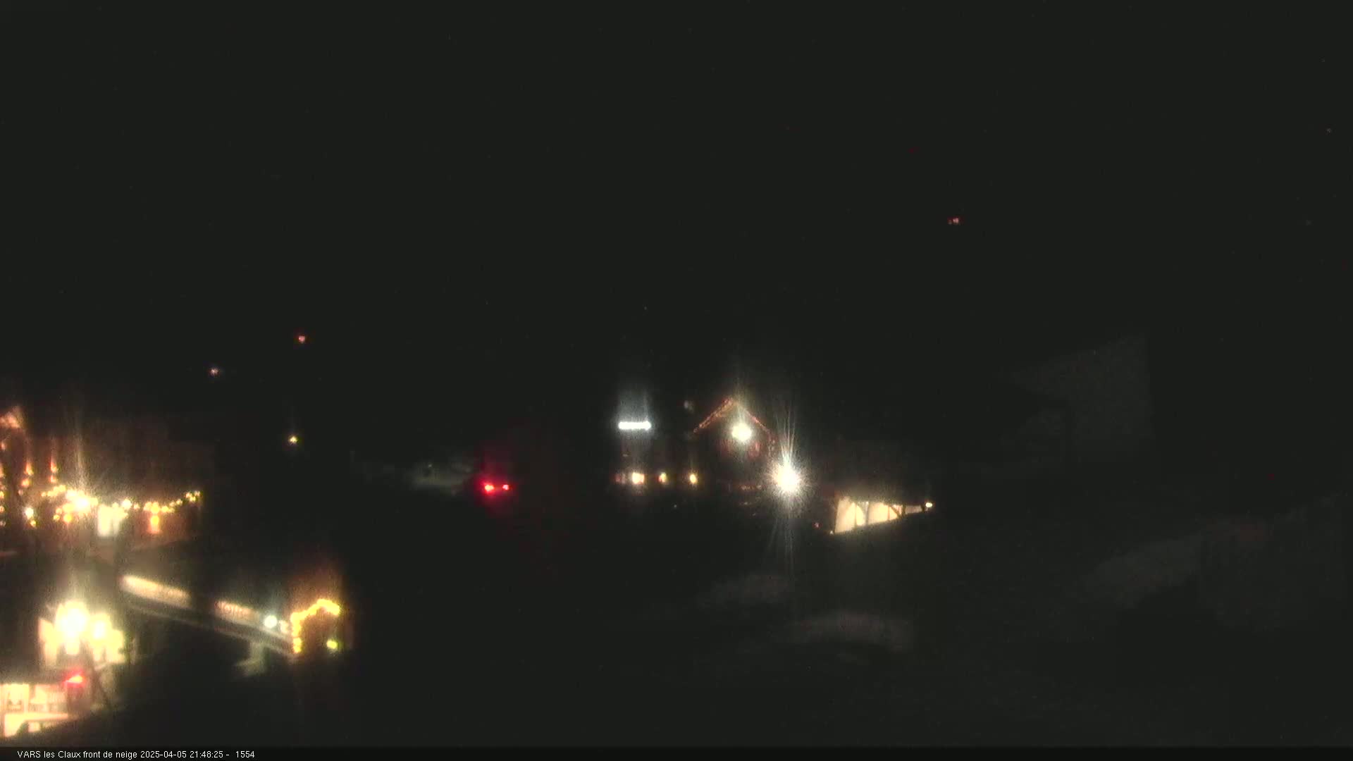 A nighttime, outdoor scene shows dimly lit buildings and vehicles with their headlights on.