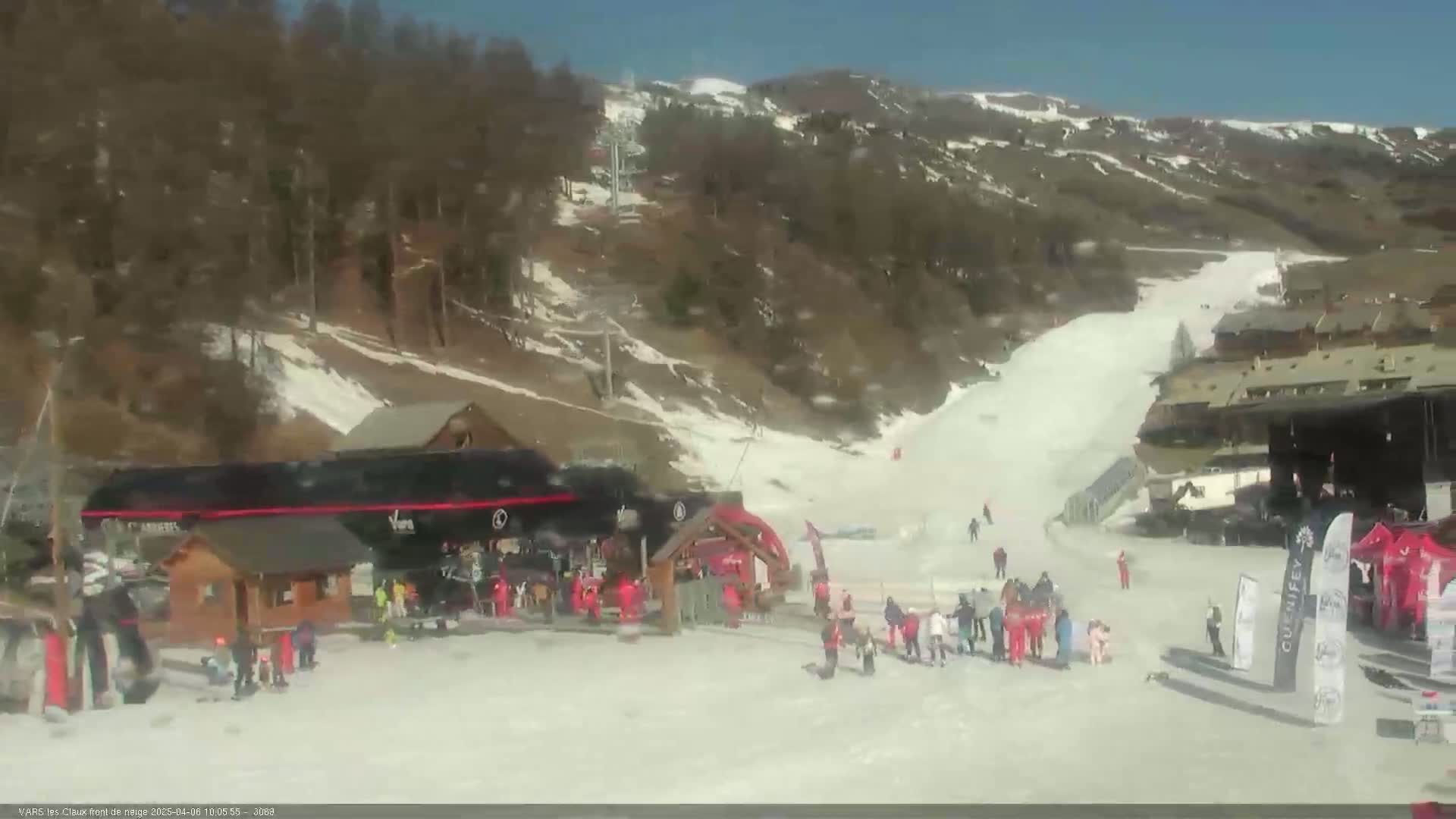 A snowy ski slope with several skiers and snowboarders near the base, under a sunny sky.