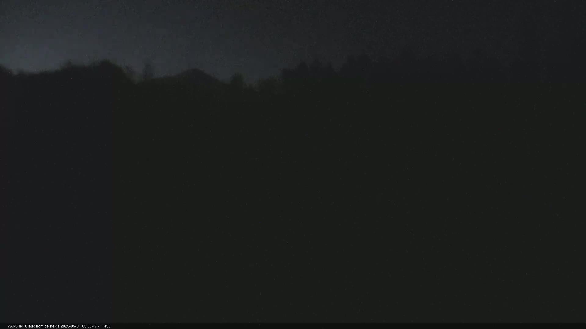 A dark, nighttime view shows a silhouetted line of trees and hills under a mostly clear sky.
