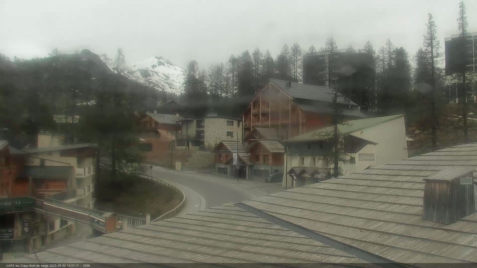 A misty mountain village scene shows several buildings and a curving road, with a snow-capped mountain in the background.