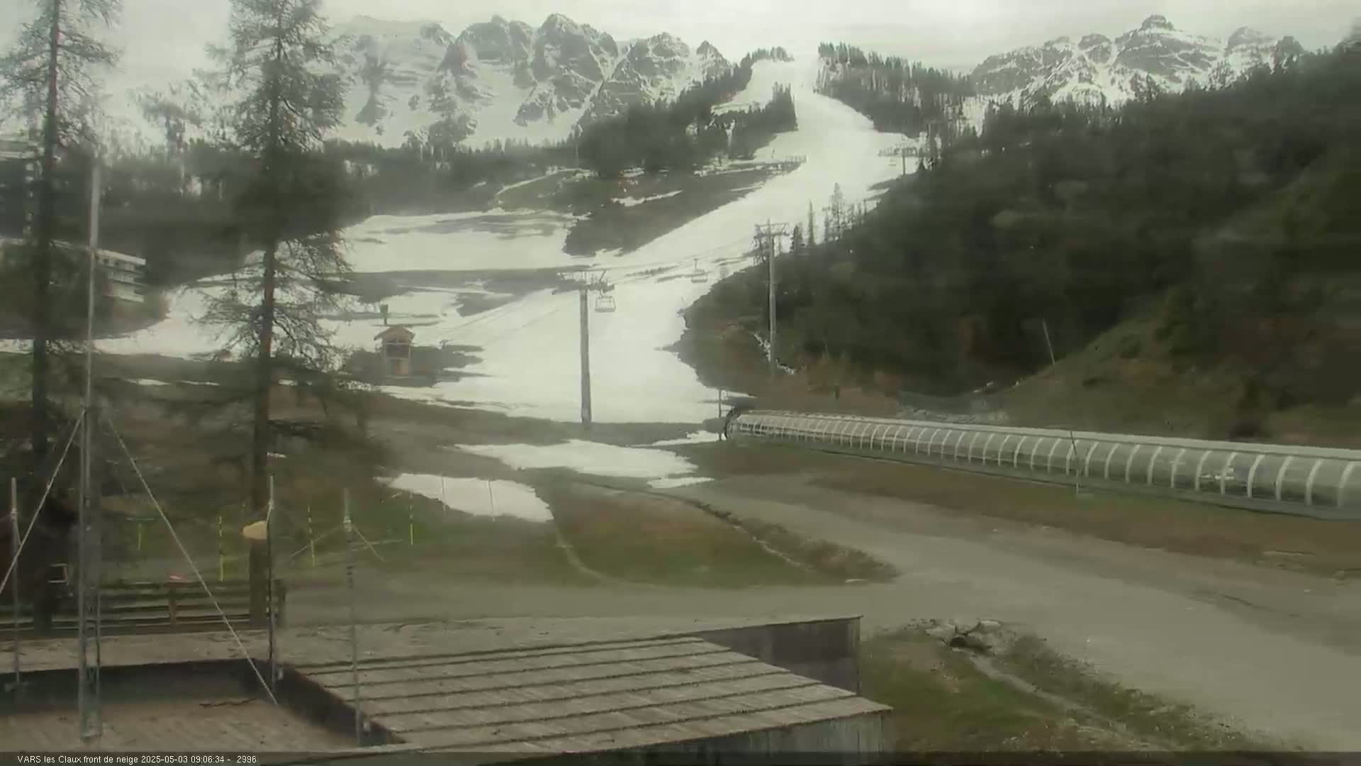 A snow-covered ski slope with chairlifts and a long, covered structure is visible under an overcast sky.