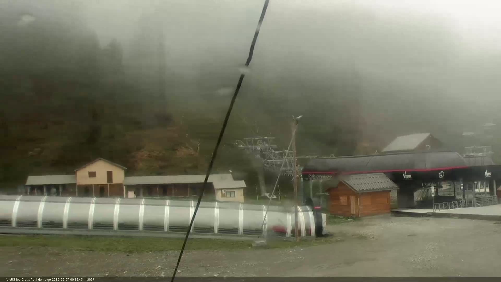A foggy mountainside scene shows a ski lift and several small buildings near a covered conveyor belt.