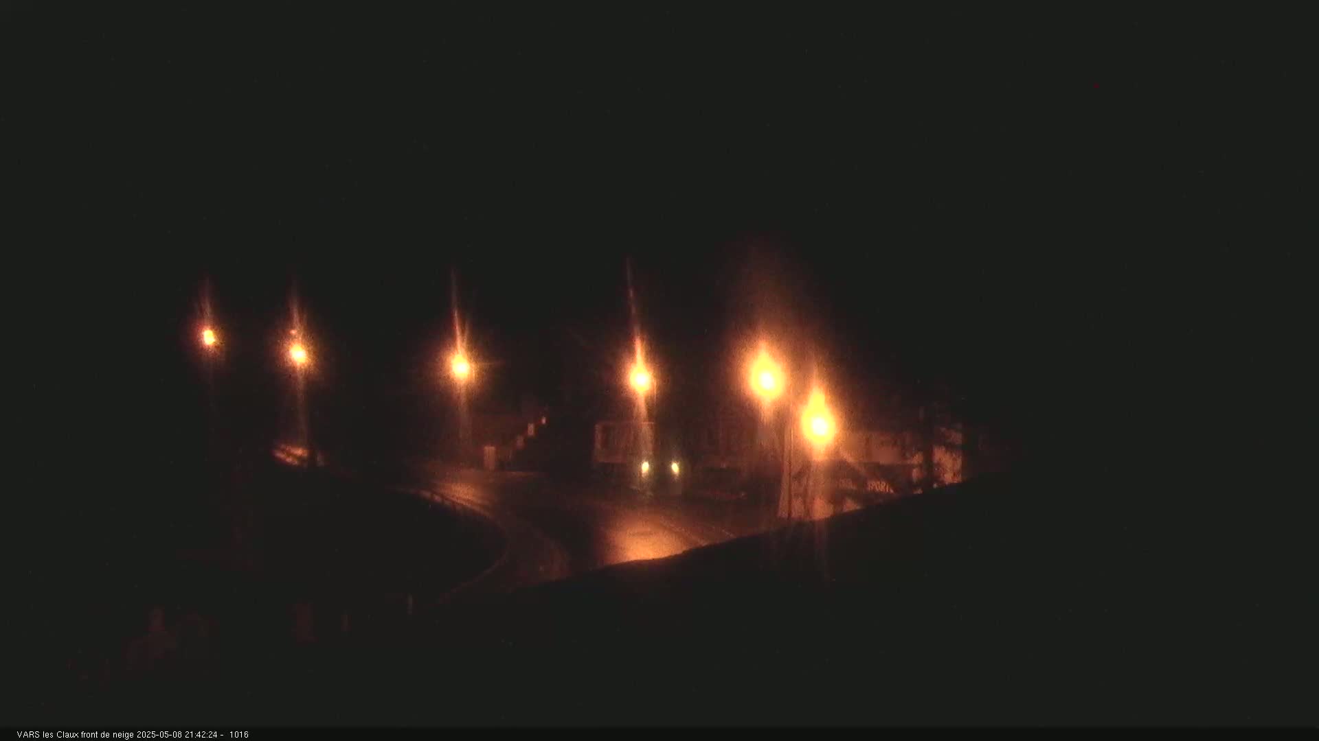 At night, several bright streetlights illuminate a dark road and nearby buildings.