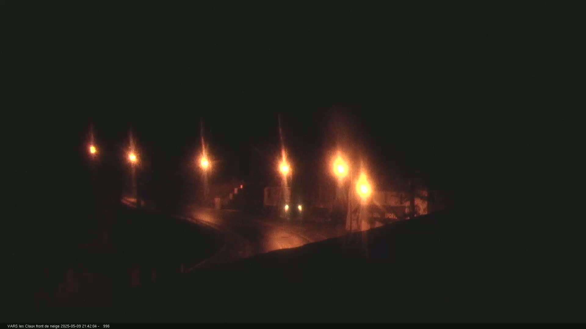 Several illuminated streetlights cast a dim glow on a dark, nighttime road.