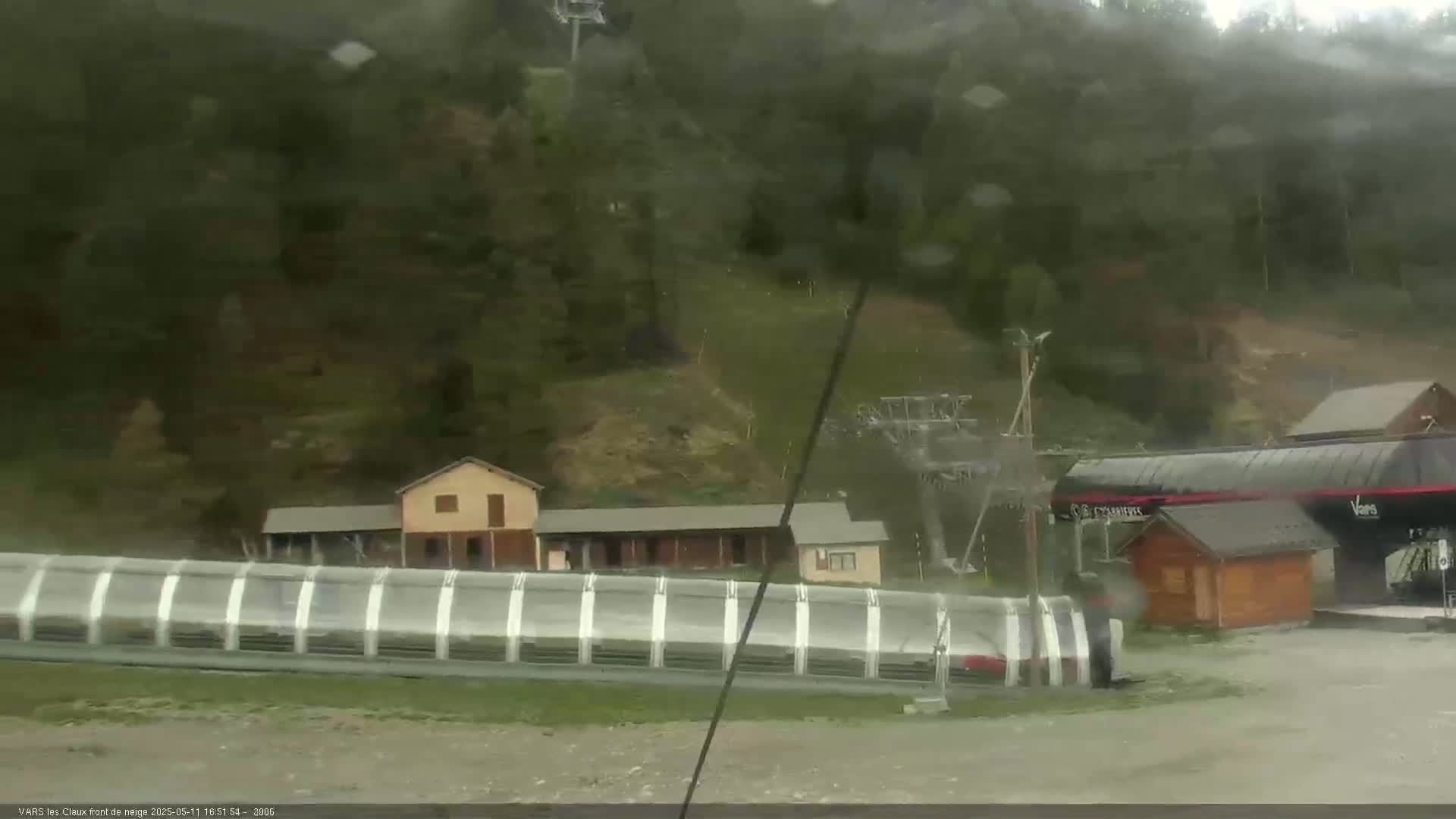 A ski lift and several buildings are visible in a rainy, wooded mountain area.