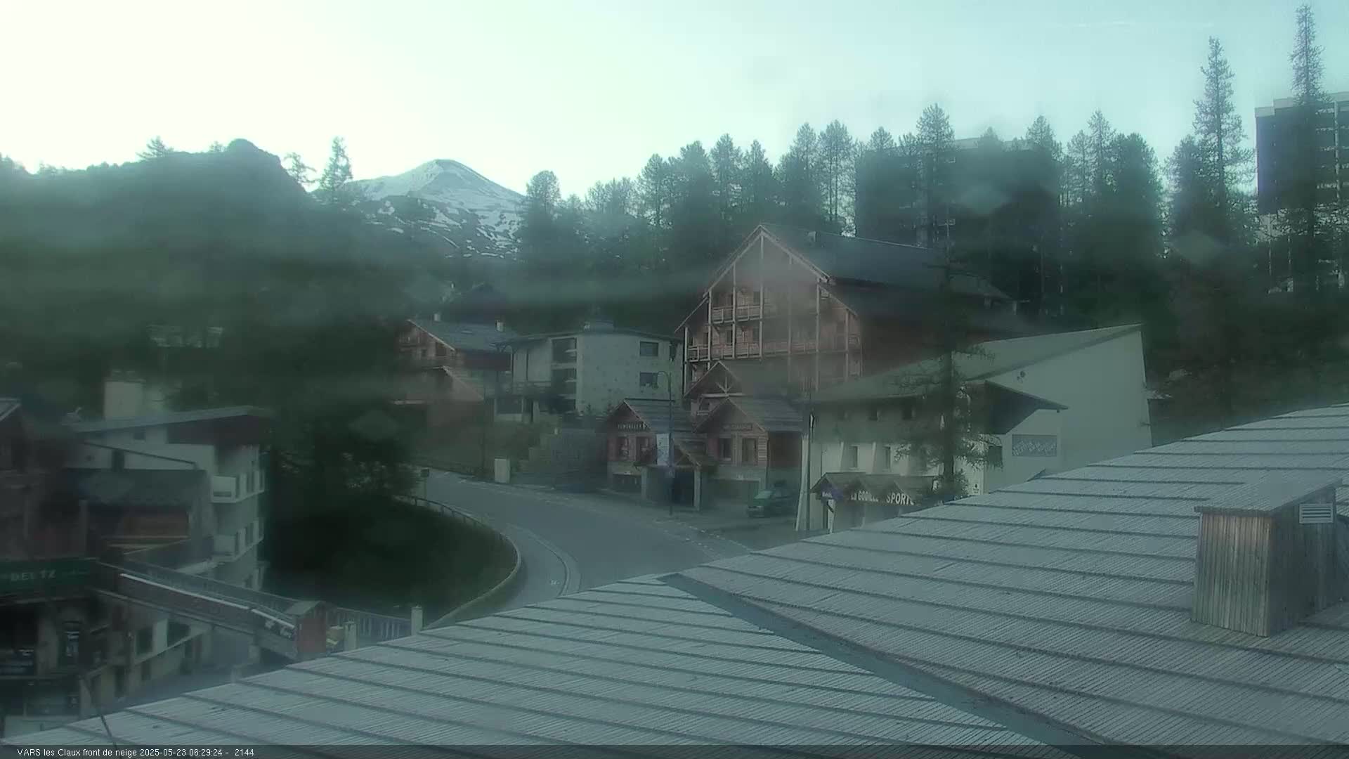 A mountain village is shrouded in mist, with snow-capped mountains visible in the distance.