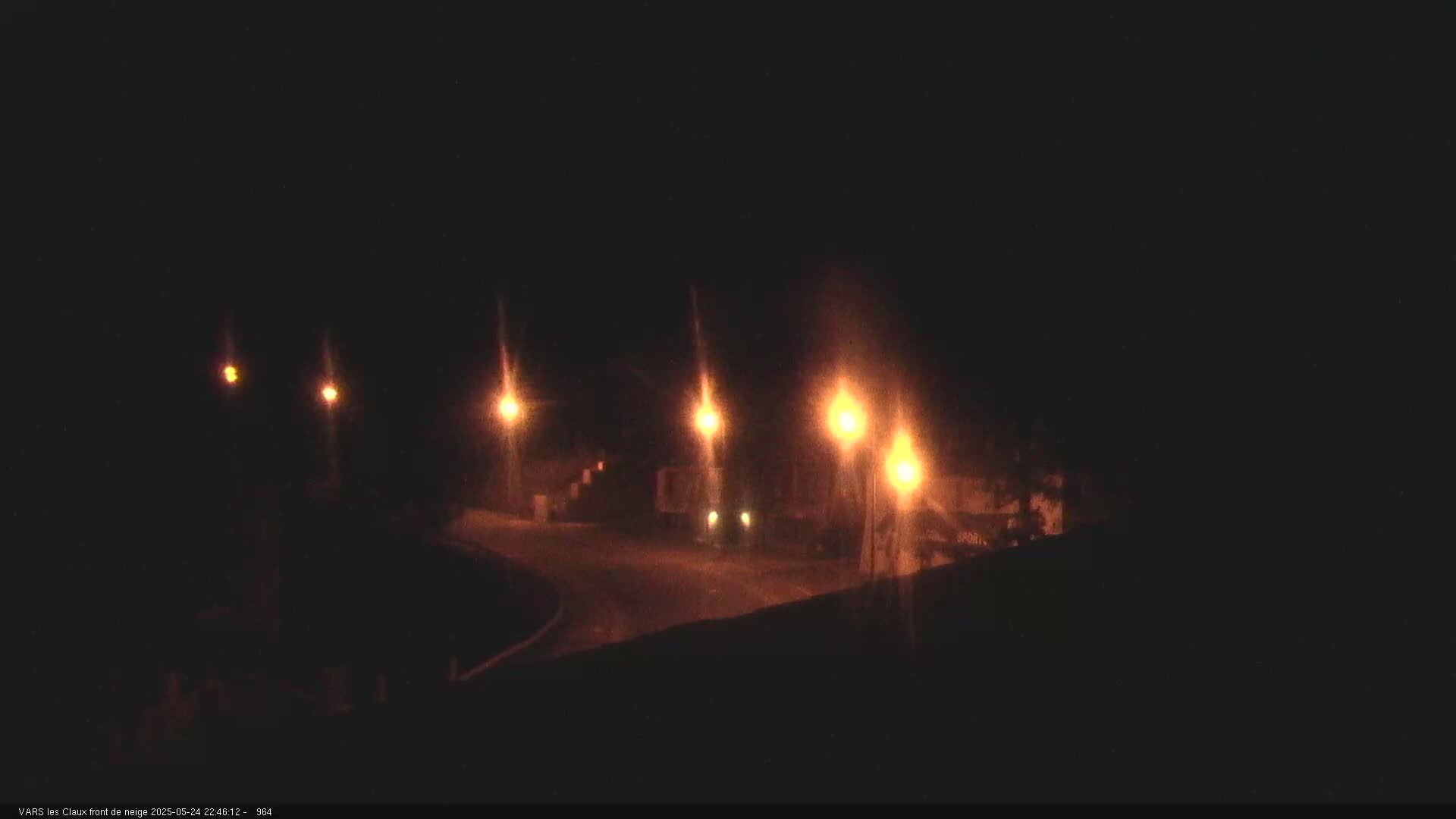 Several dimly lit streetlights illuminate a dark, nighttime road curving gently to the left.