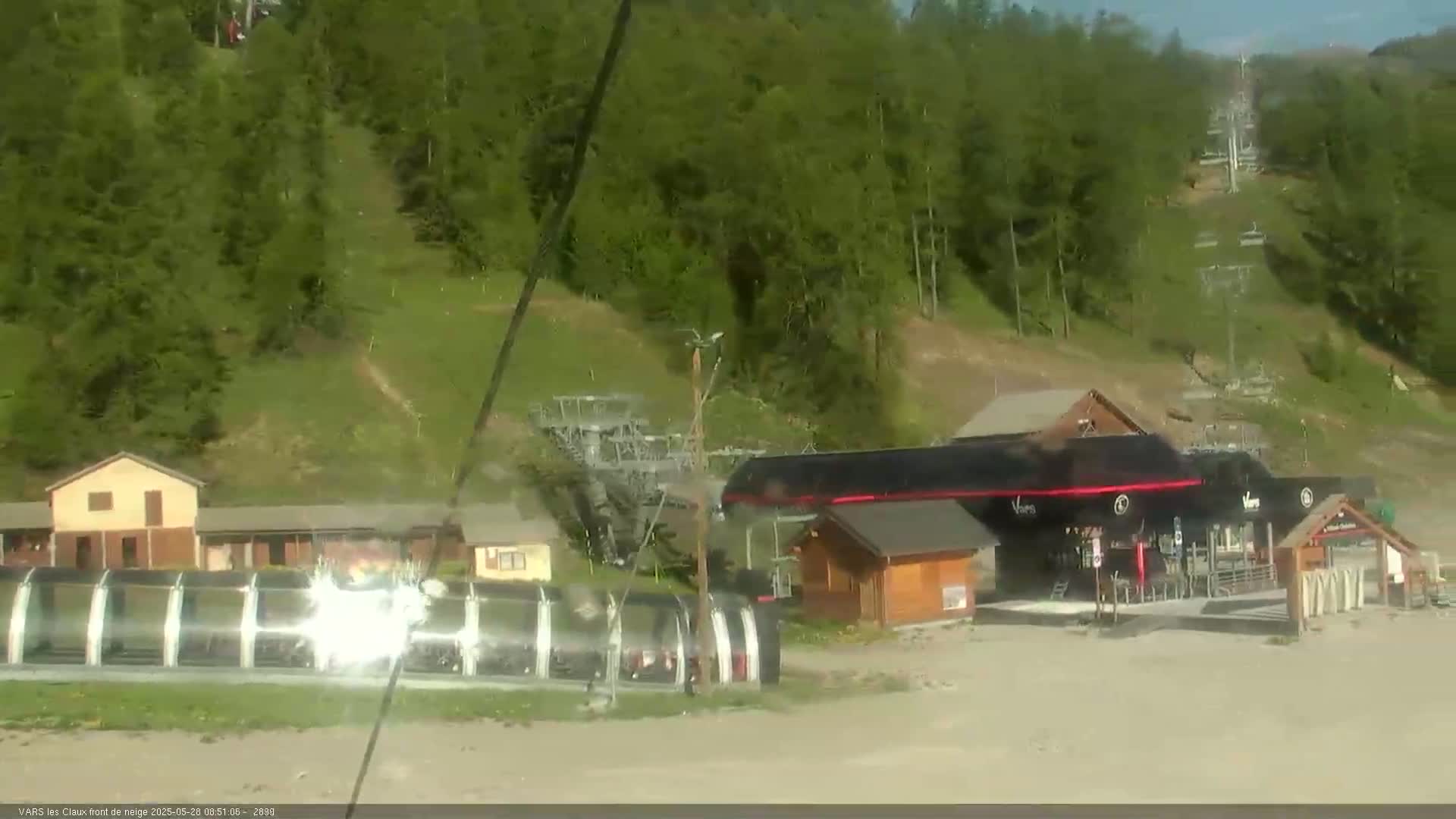 A ski resort base area with buildings, chairlifts, and a grassy hillside under a mostly clear sky.