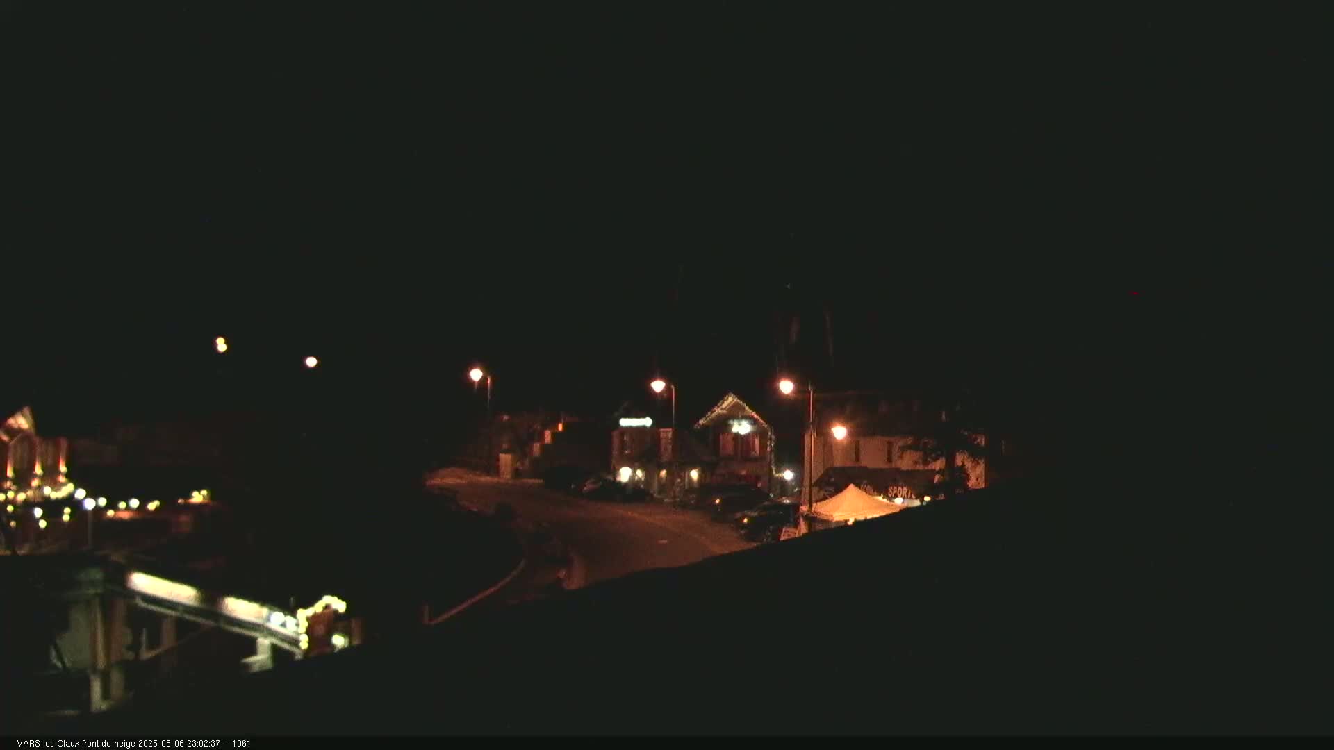 A nighttime view of a small town street with a few buildings illuminated by streetlights under a clear, dark sky.