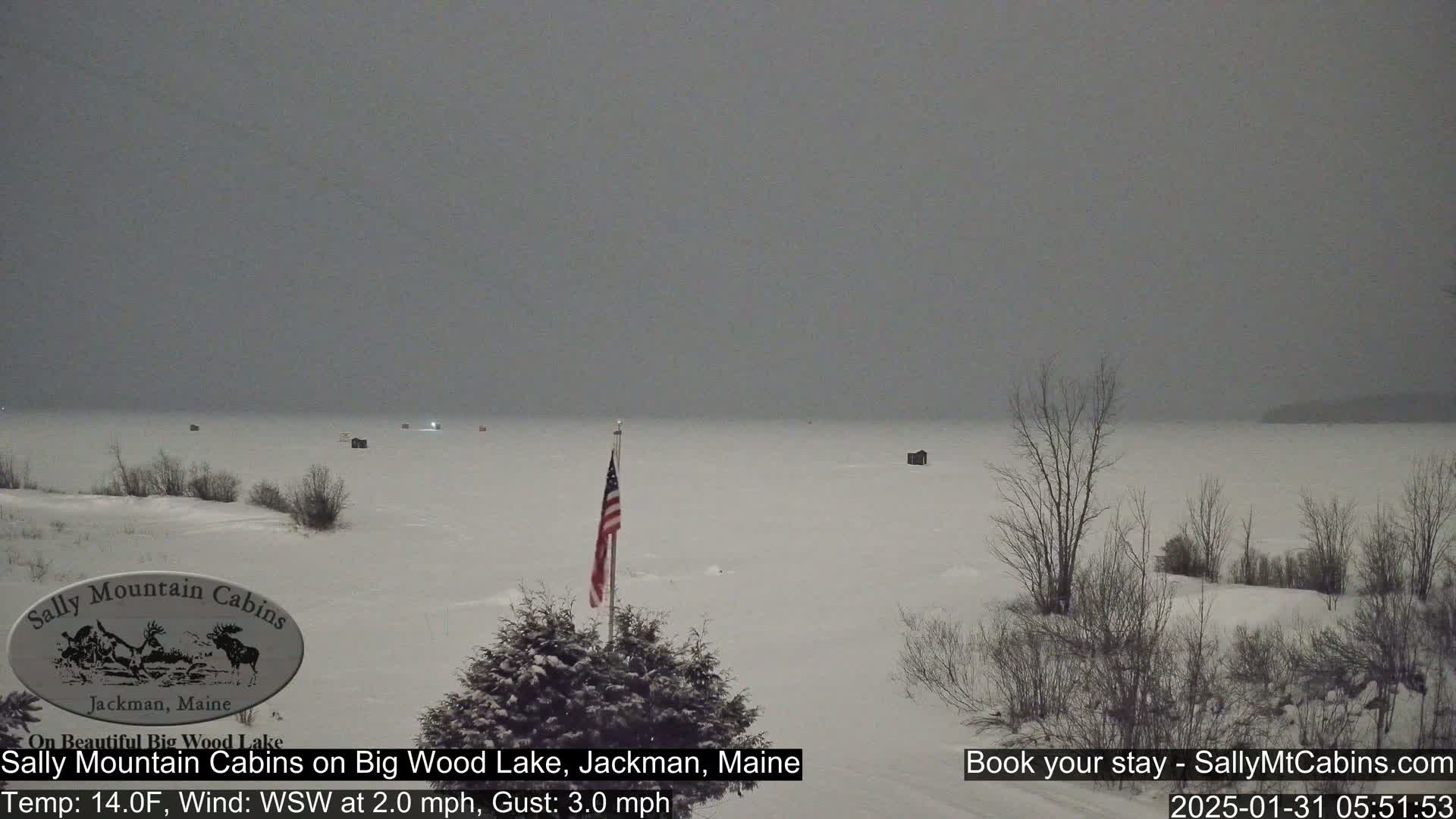 A snow-covered frozen lake with several small structures and a lone American flag is visible under an overcast sky.
