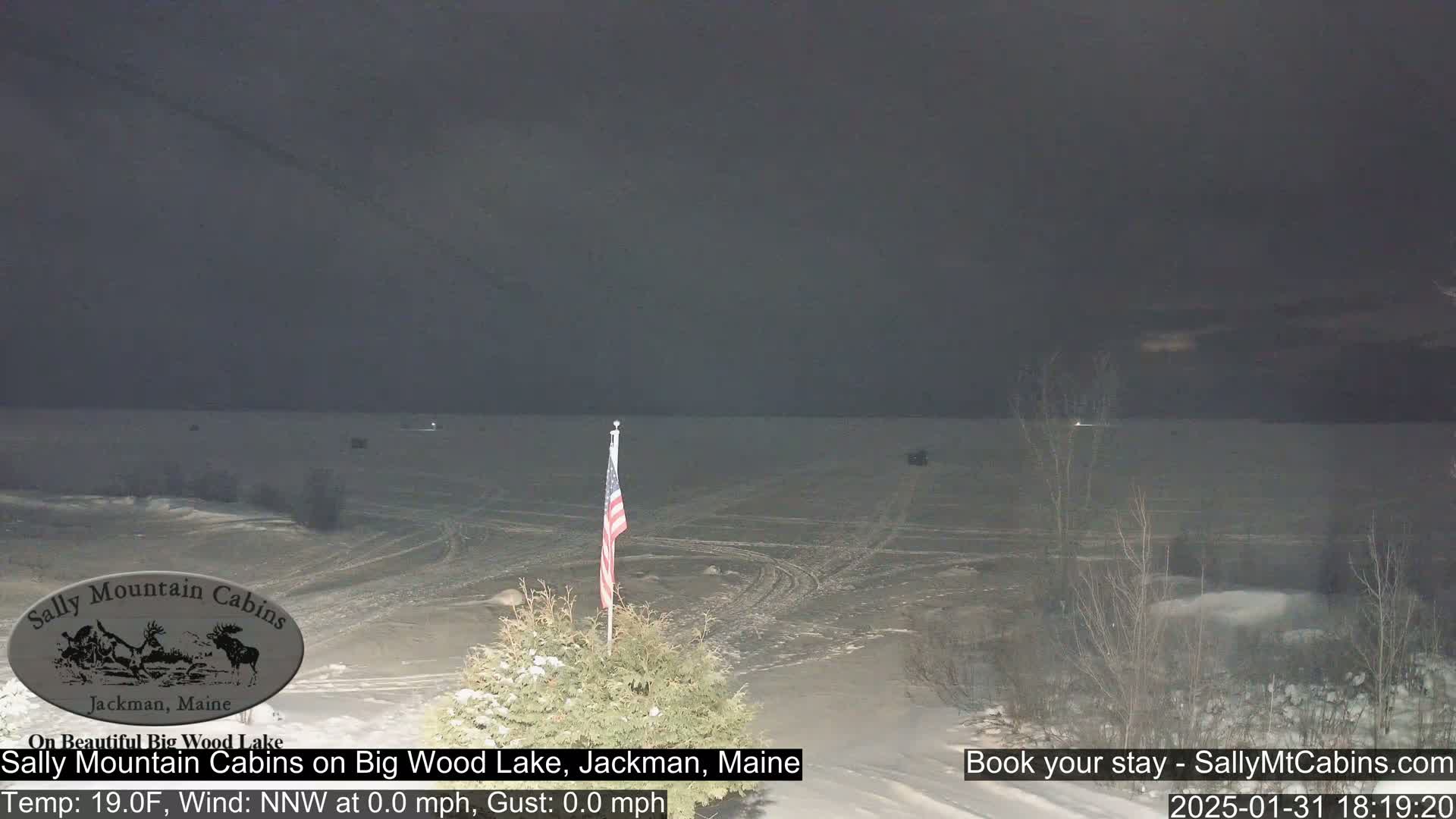 A snow-covered lake is seen at night under a dark sky, with a small American flag in the foreground.