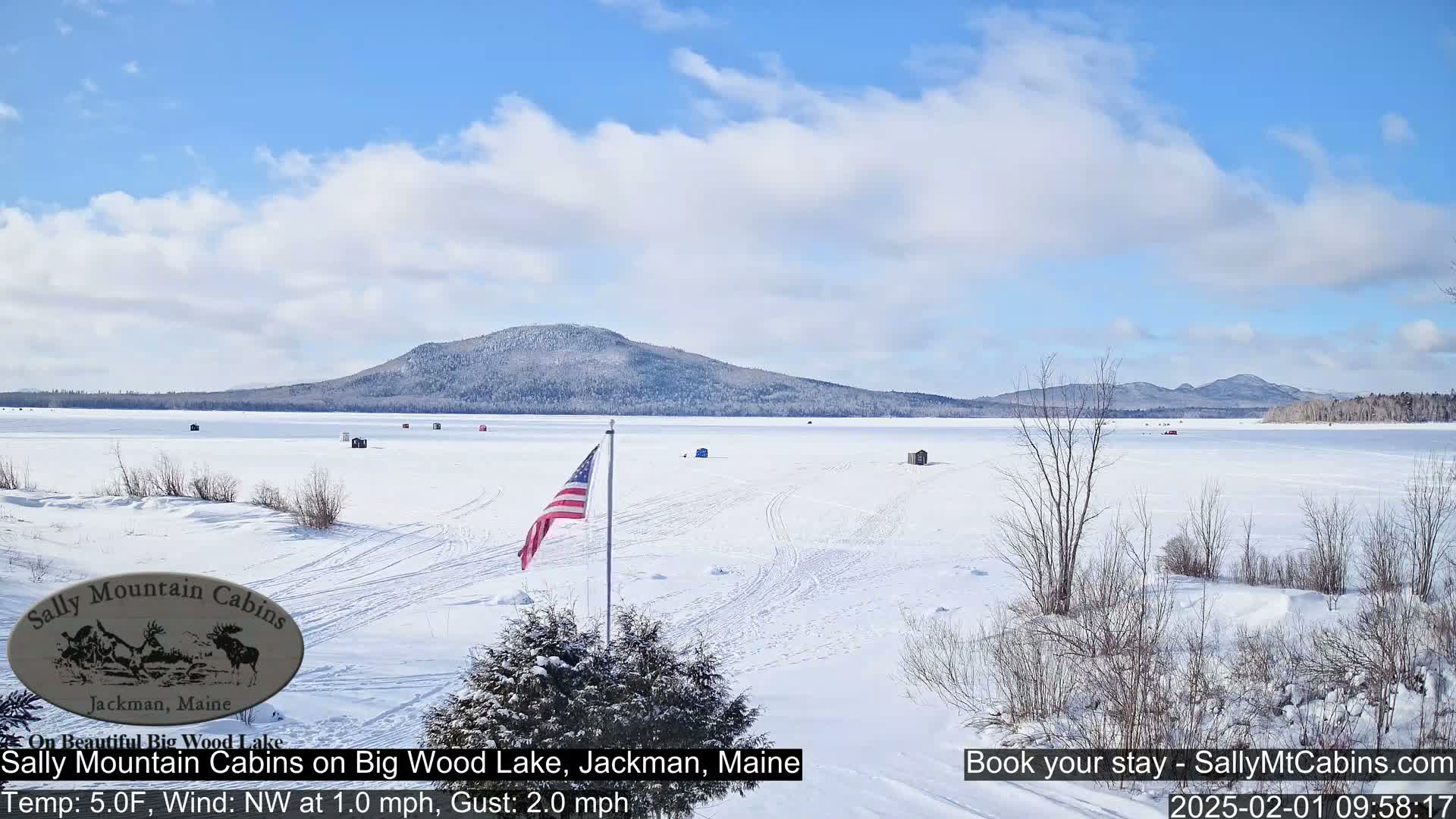 A snow-covered frozen lake stretches towards a distant, snow-dusted mountain under a mostly sunny sky.