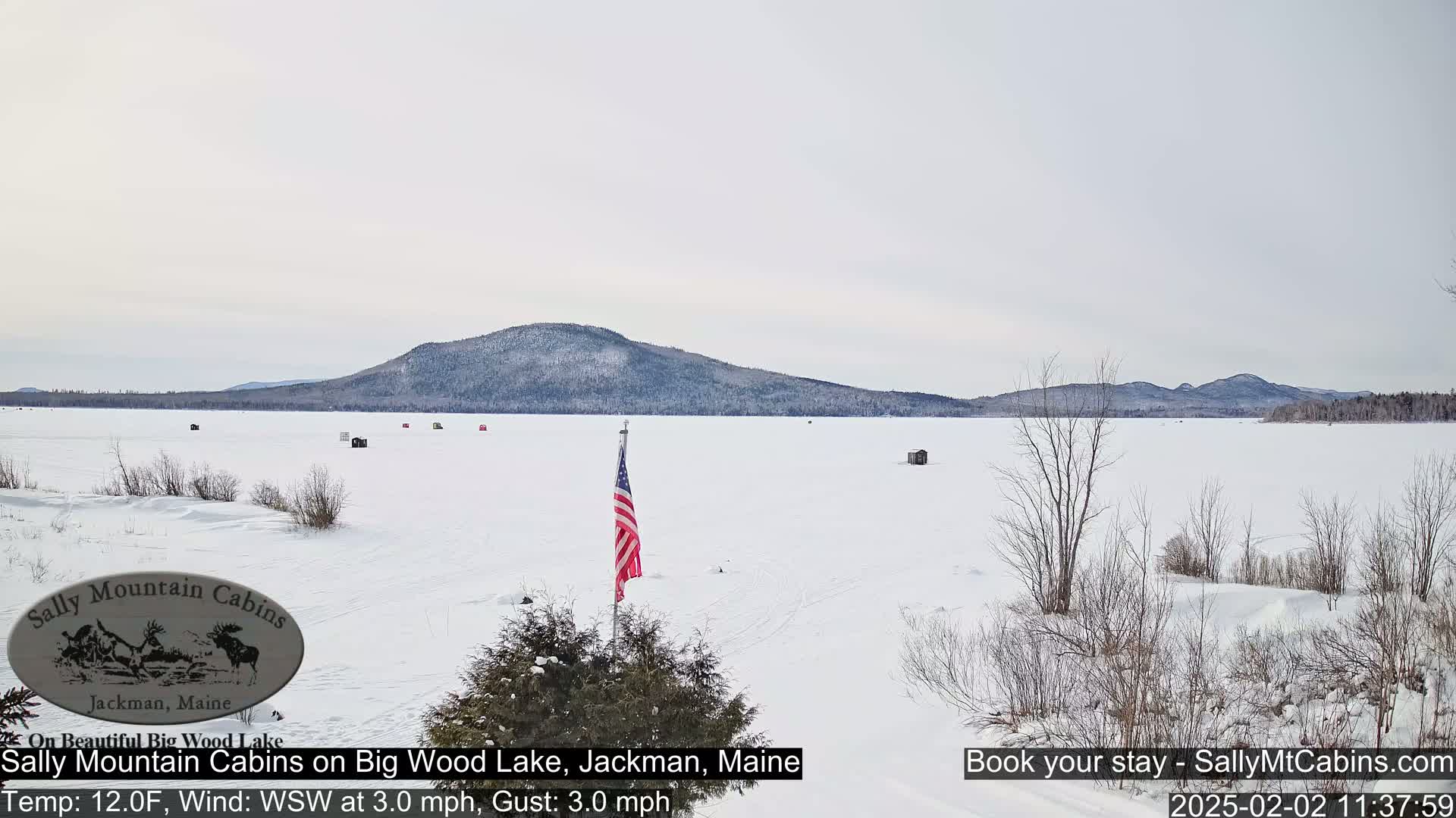 A snow-covered frozen lake stretches to a distant, snow-capped mountain range under a cloudy sky.