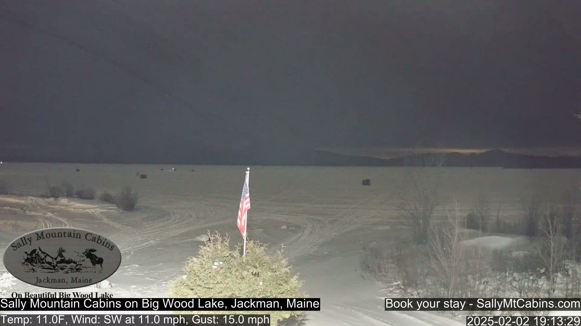 A snow-covered landscape shows a frozen lake under a dark, overcast sky with a small American flag in the foreground.