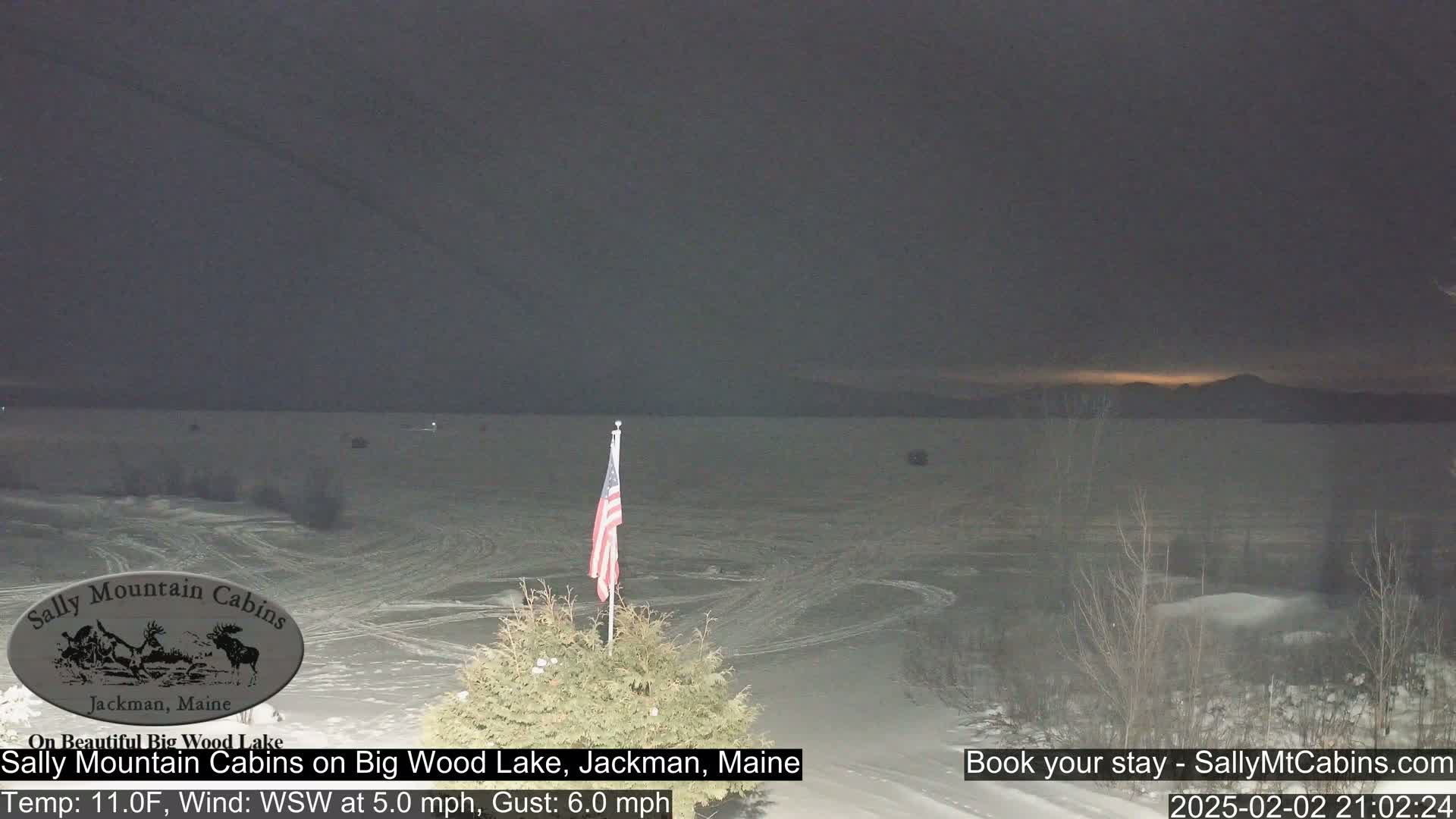 A snow-covered lake is visible under a dark, twilight sky with a faint glow on the horizon, and an American flag stands in the foreground.