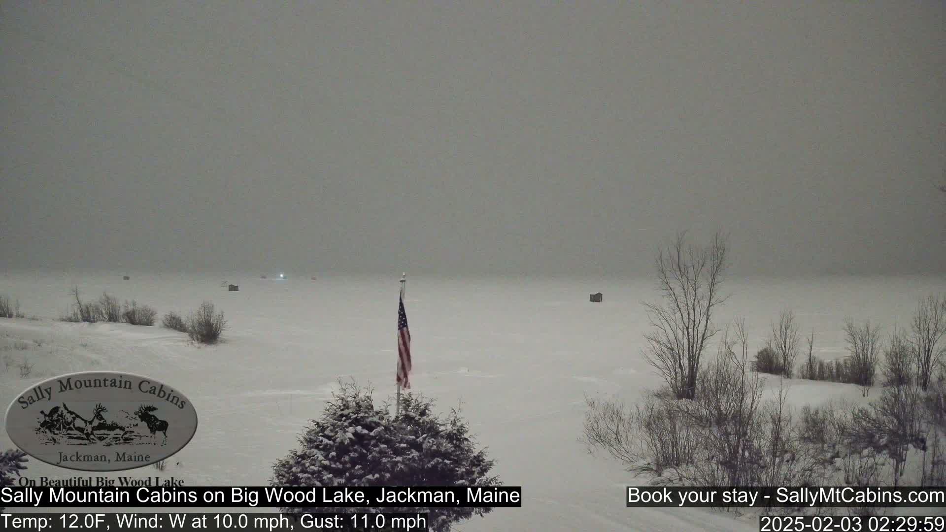 A snow-covered lake with a few small structures visible in the distance under an overcast sky.