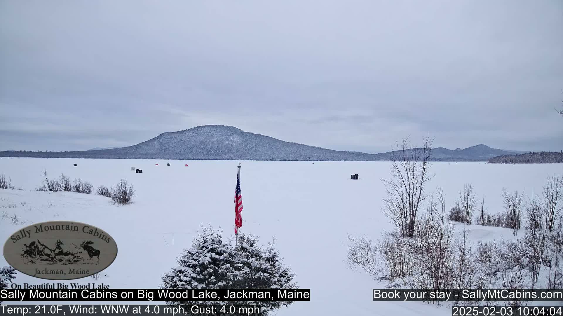 A snow-covered frozen lake stretches to a snow-dusted mountain range under an overcast sky.