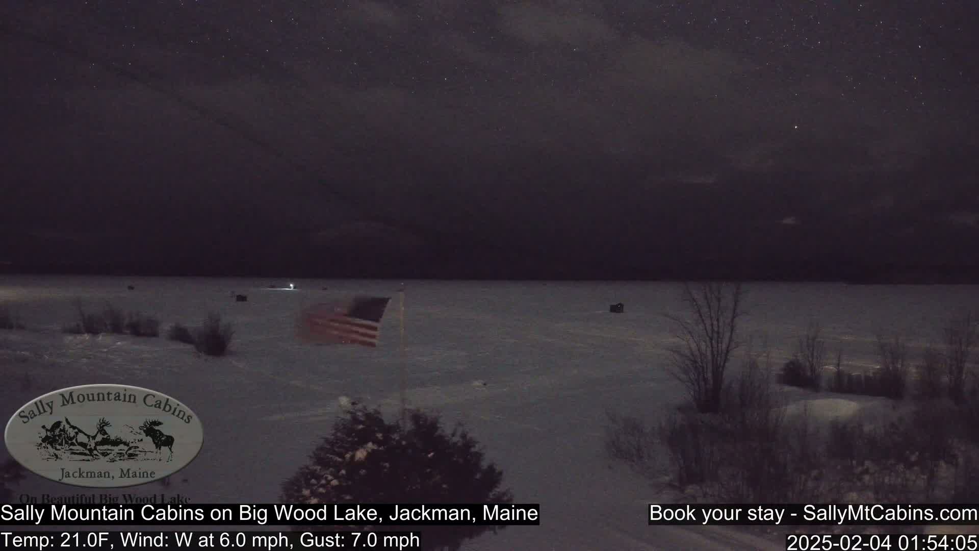 A partially frozen lake is visible under a starry night sky with a light westerly wind.