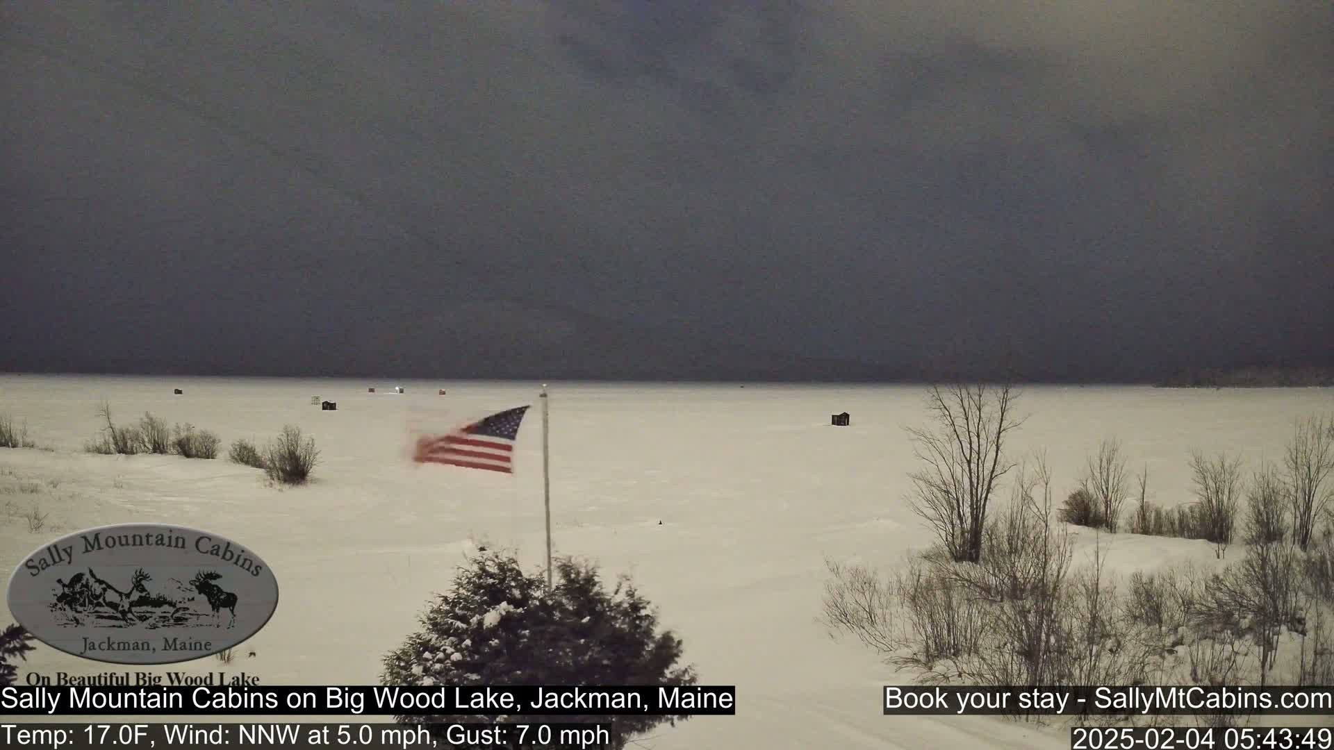 A snow-covered frozen lake is visible under a dark, overcast sky with an American flag waving in the foreground.