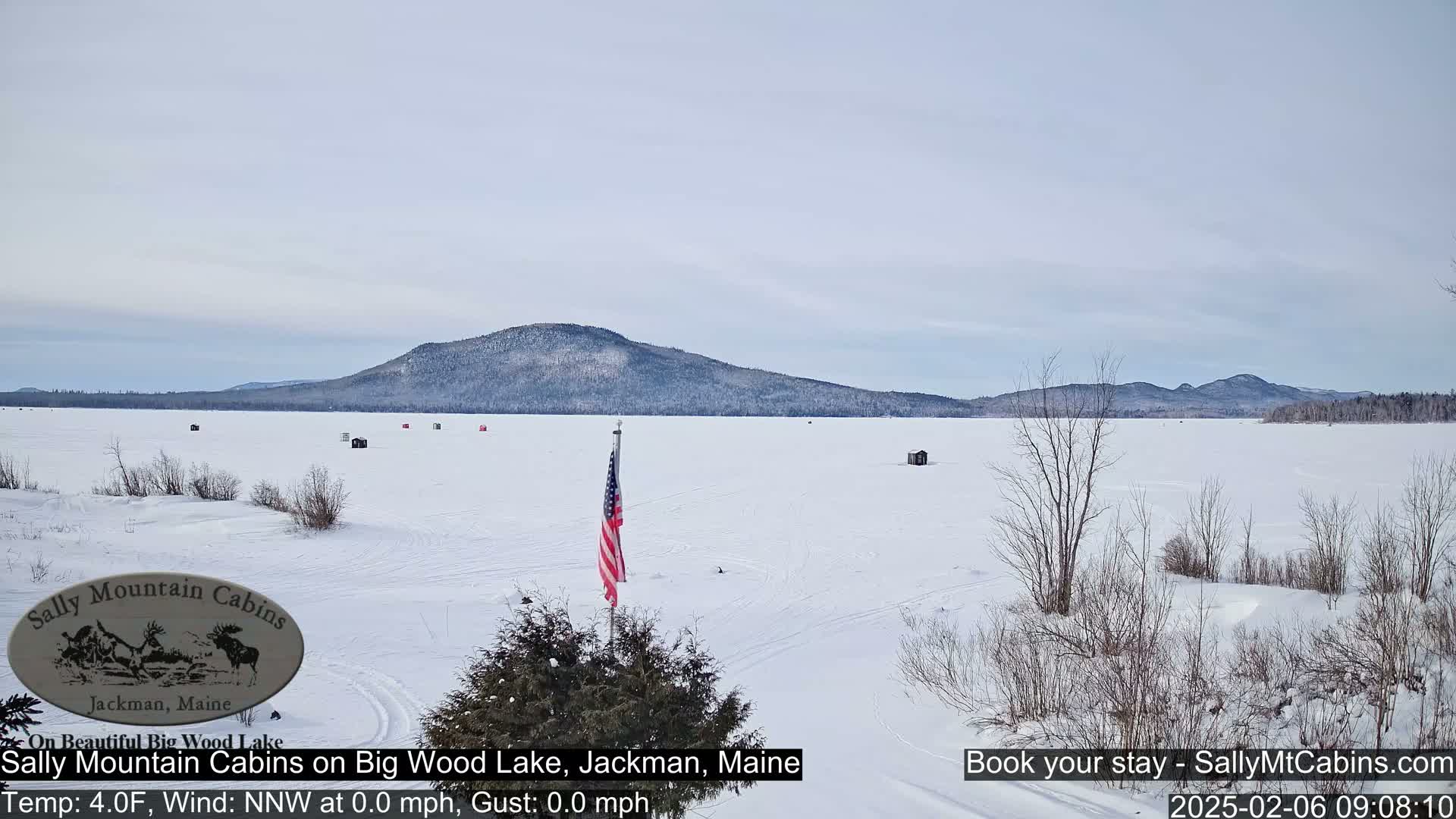 A frozen lake stretches towards a snow-covered mountain range under a pale sky.