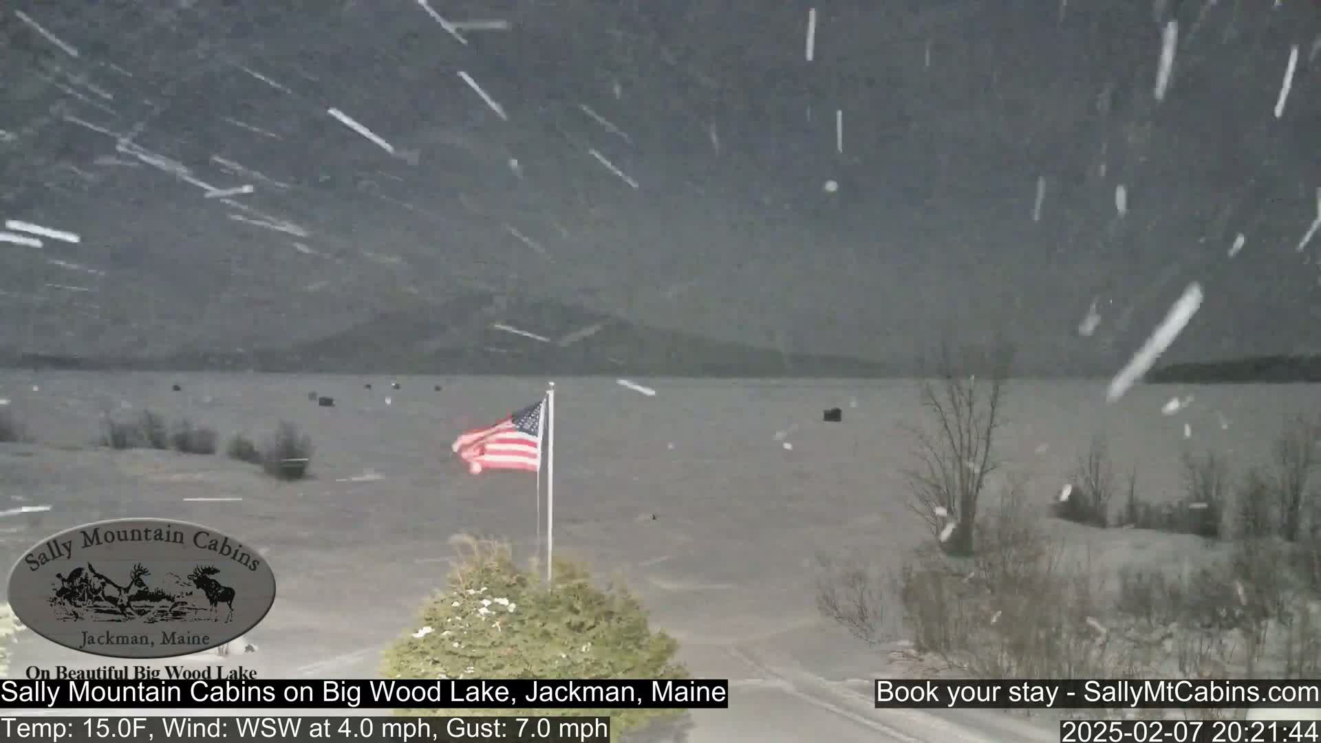 A snow-covered landscape with a lake in the background, under heavy snowfall, with an American flag waving in the wind.