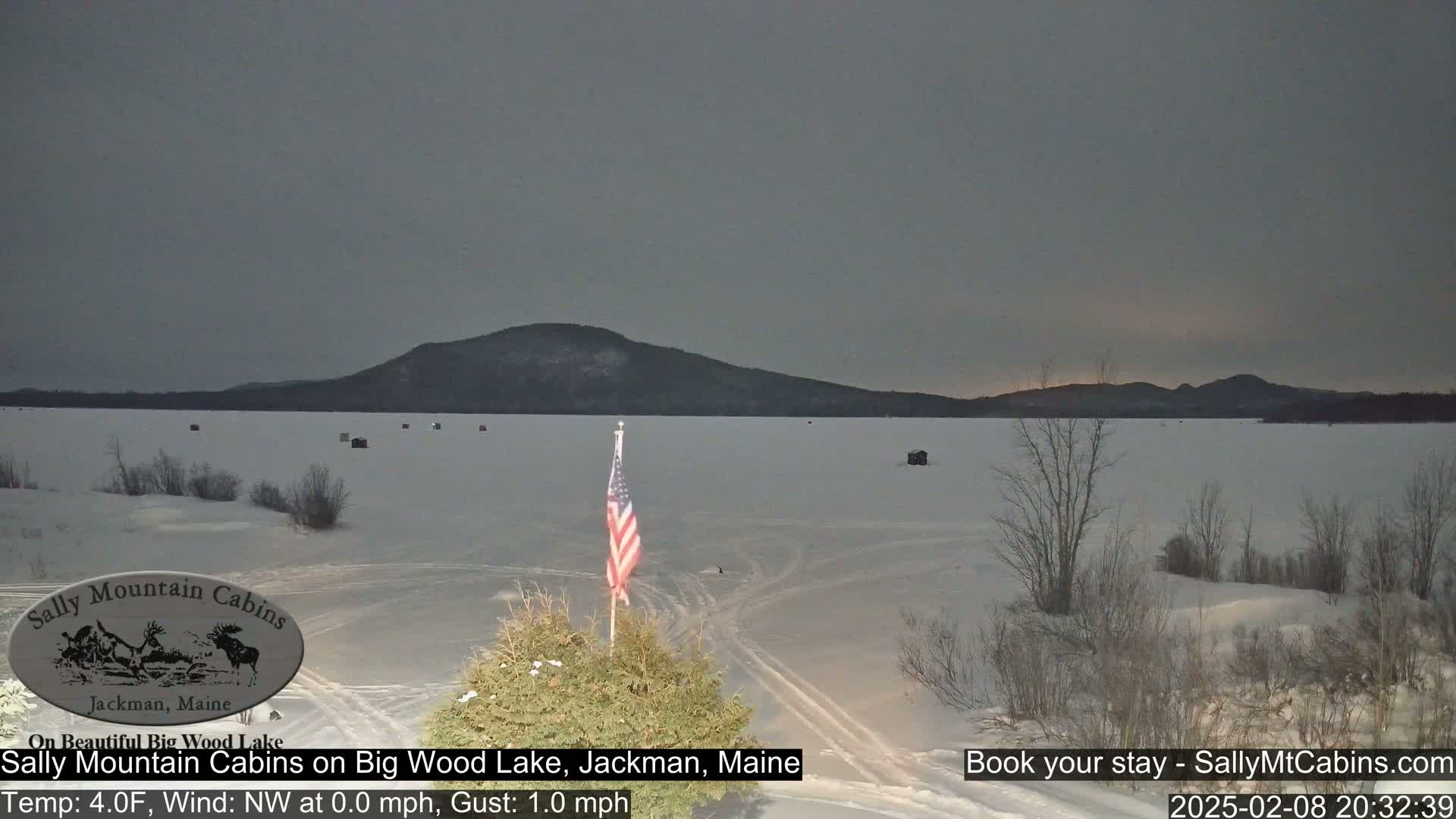 A frozen lake under a gray sky, with a distant mountain range in the background and an American flag in the foreground.