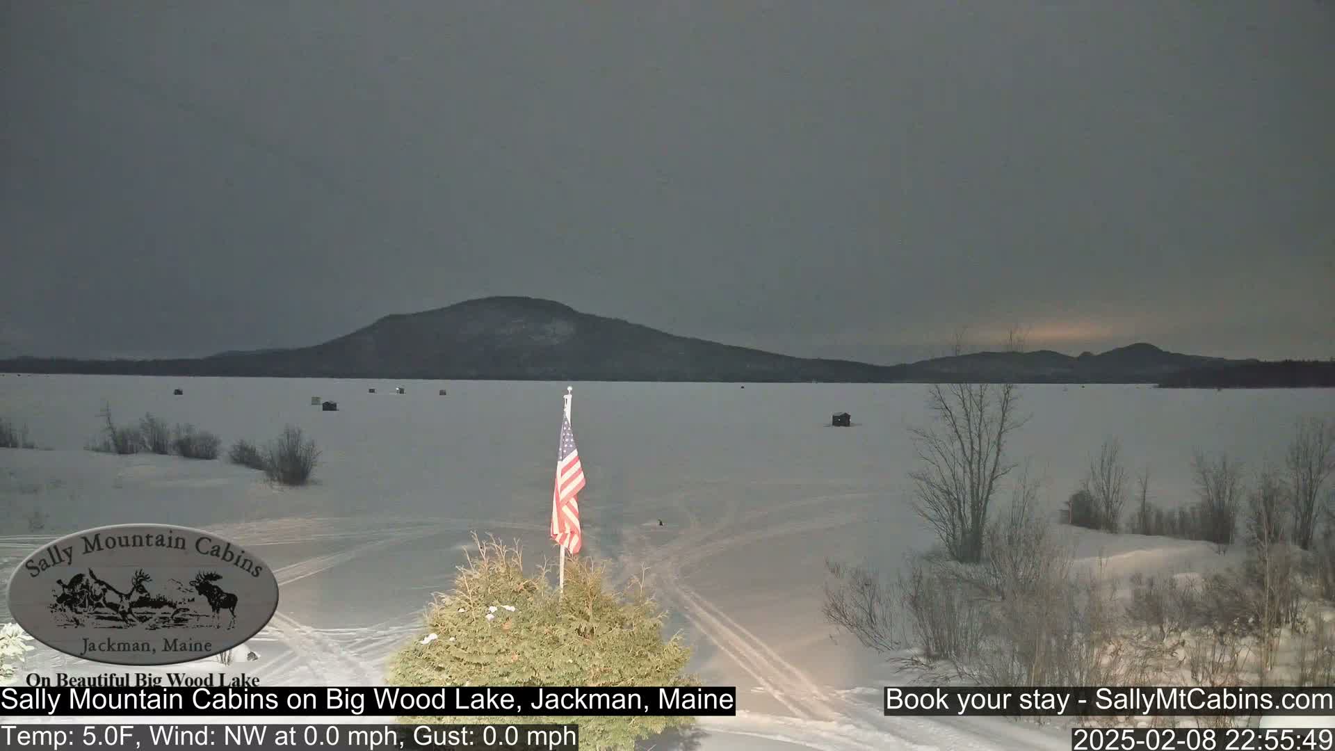 A snow-covered frozen lake stretches to a dark mountain range under a gray, overcast sky.