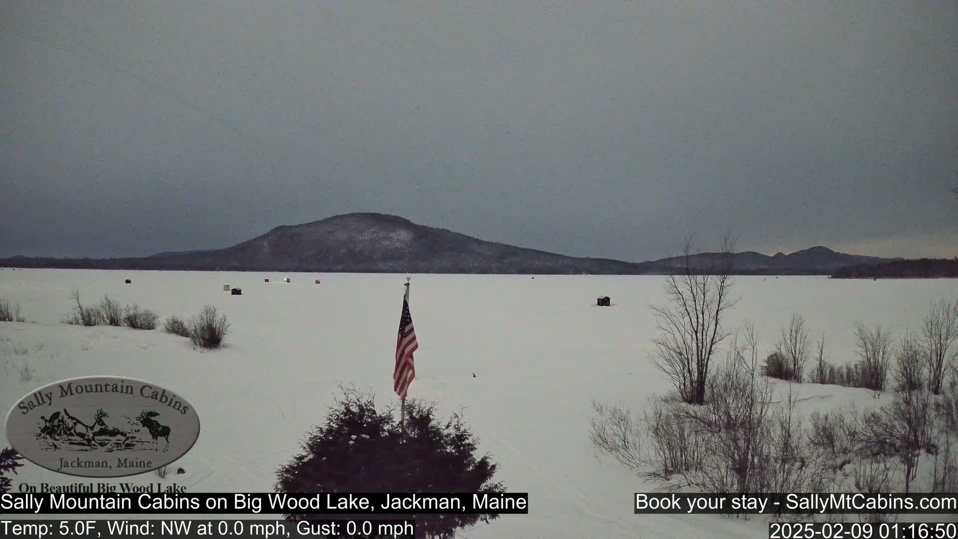 A frozen lake stretches out to a distant, snow-covered mountain range under a gray sky.