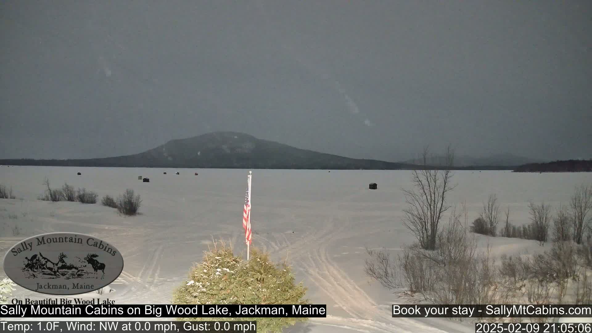 A frozen lake stretches out to a dark, snow-covered mountain under a gray, overcast sky.