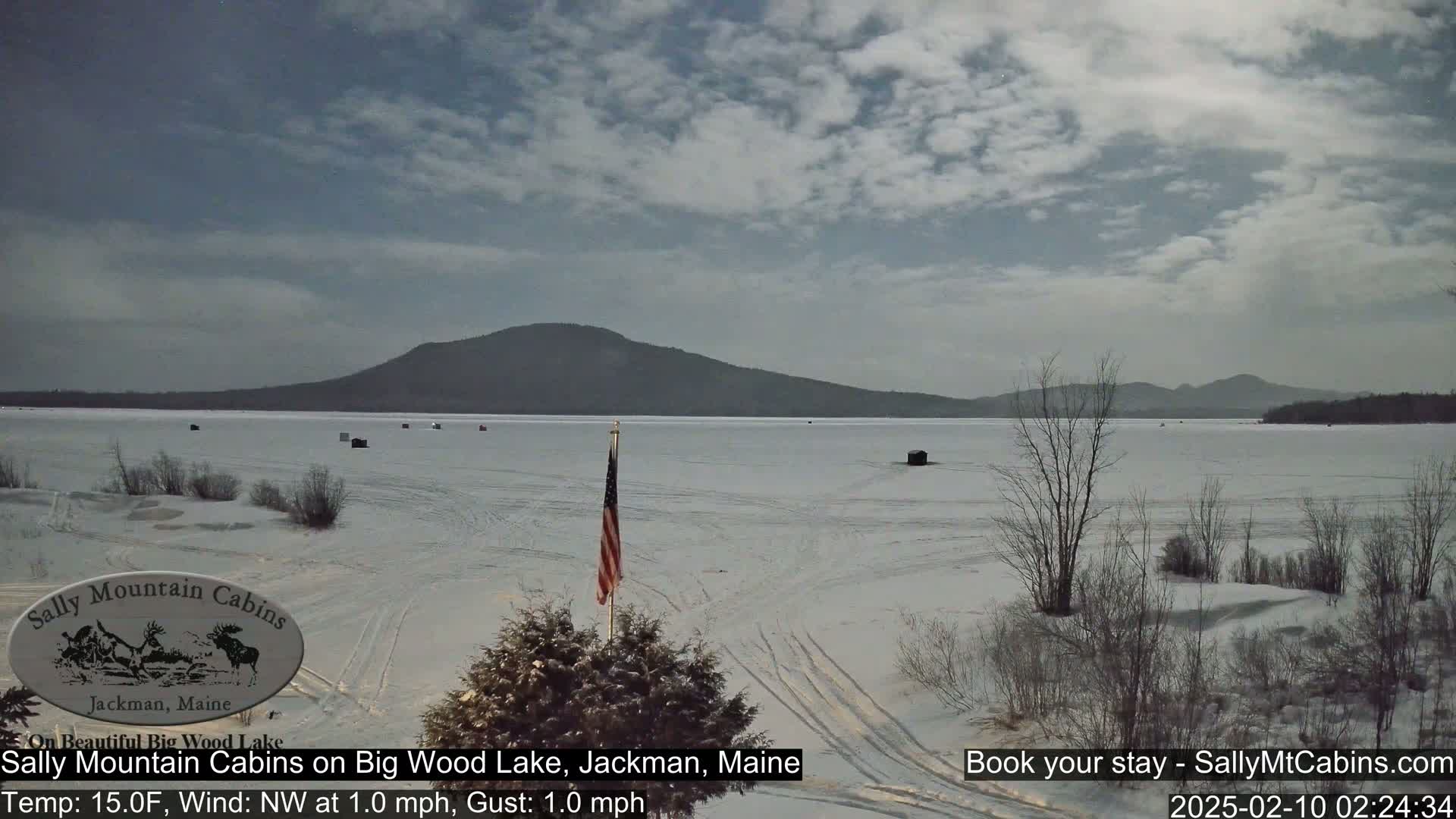 A snow-covered frozen lake stretches to a distant mountain range under a partly cloudy sky.
