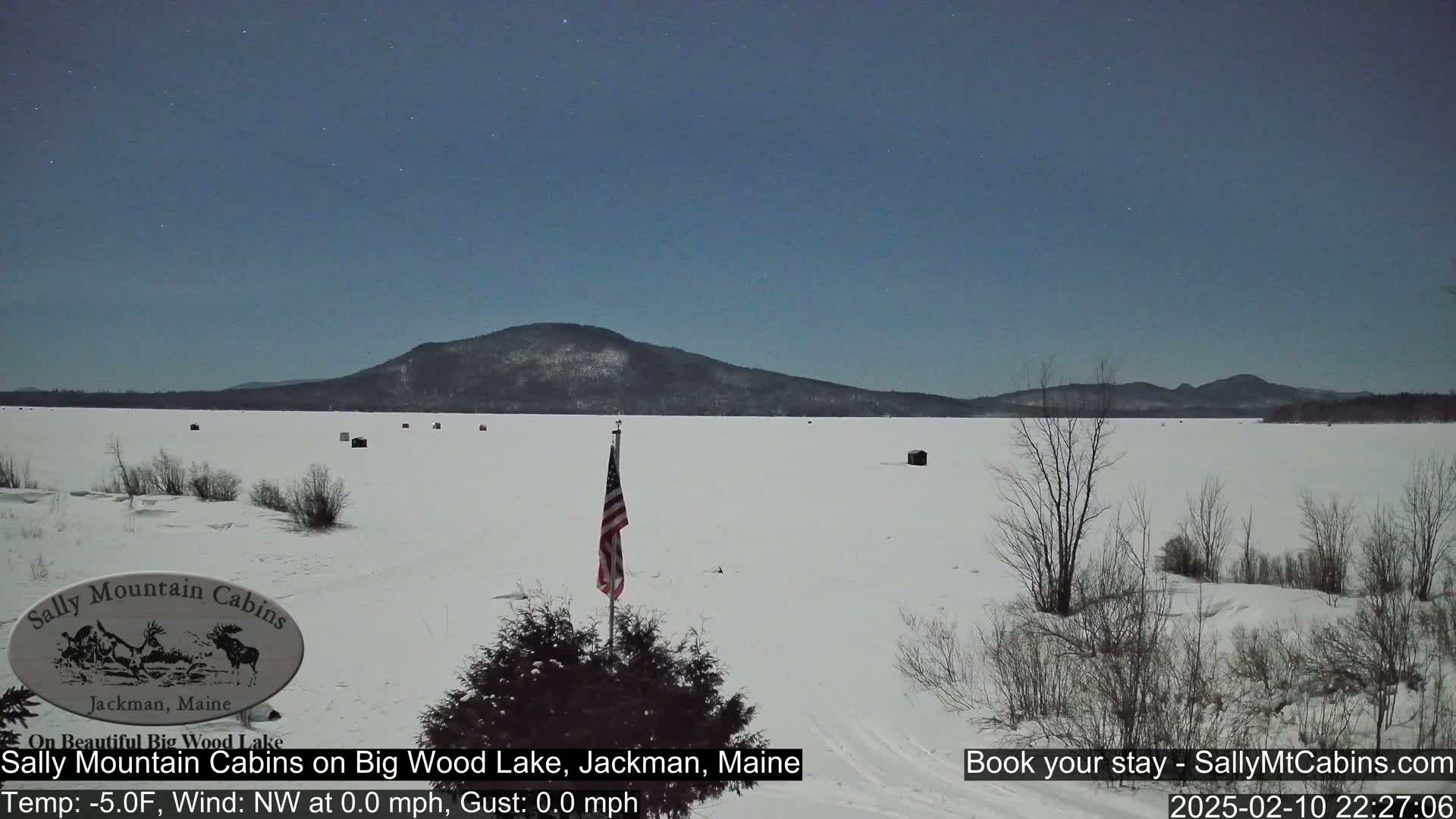 A snow-covered frozen lake stretches to a distant mountain range under a clear, starlit night sky.