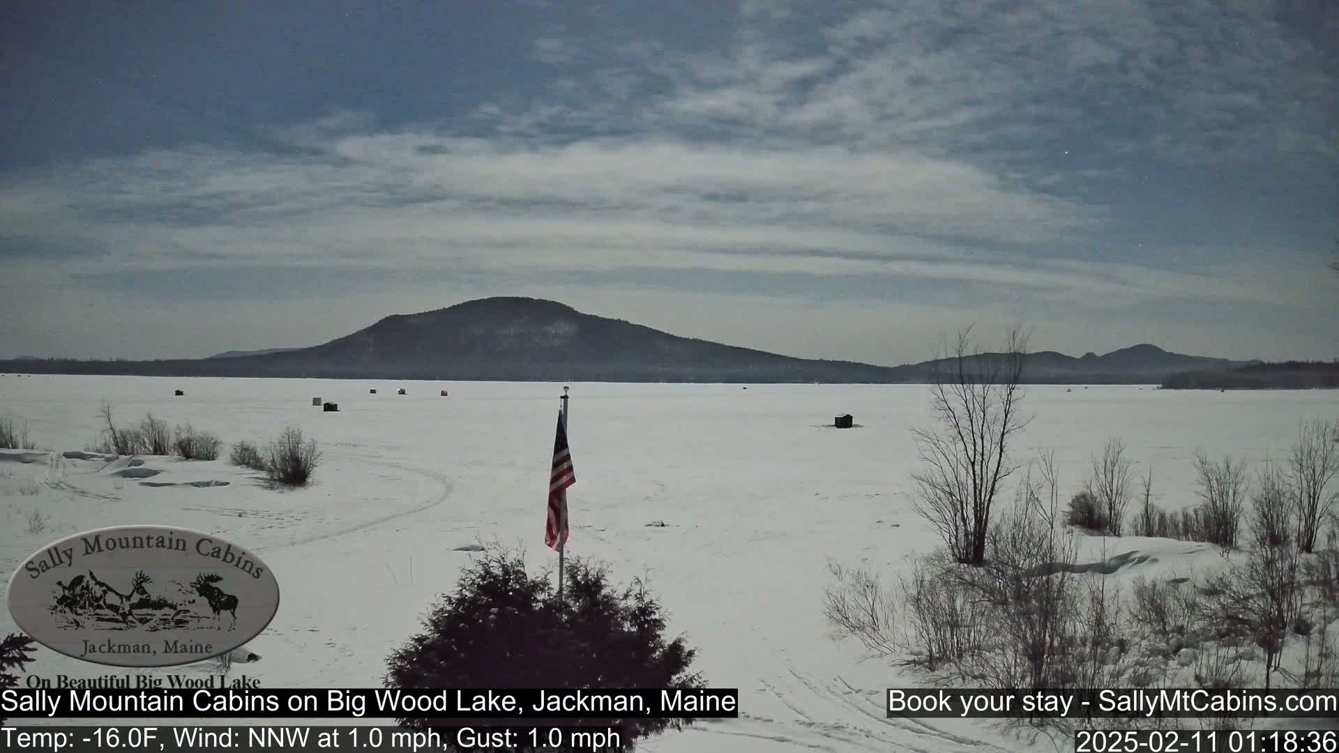 A snow-covered frozen lake stretches to a distant mountain range under a mostly cloudy sky.